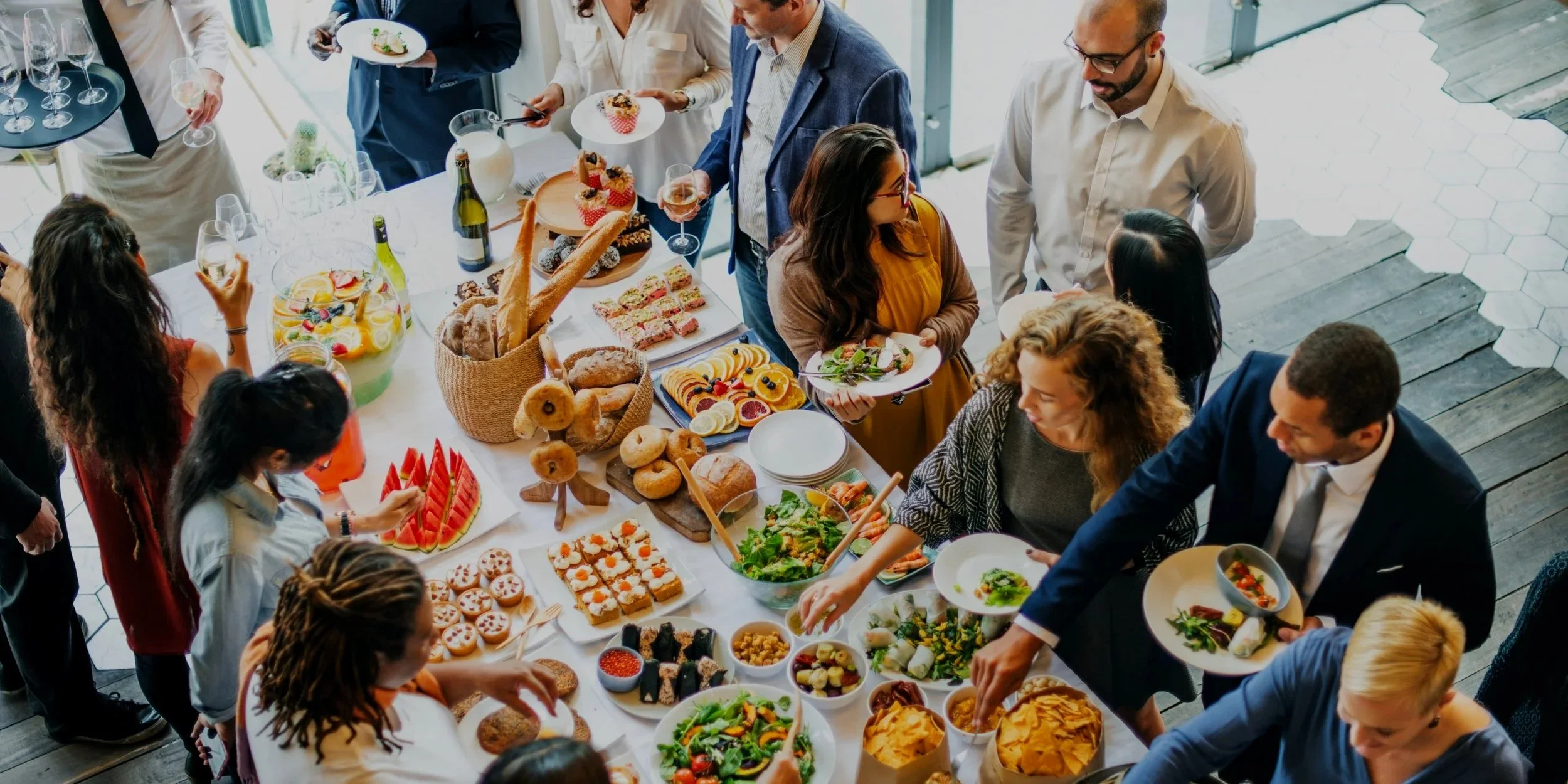 People at a buffet table with various dishes, desserts, and drinks during a social gathering.