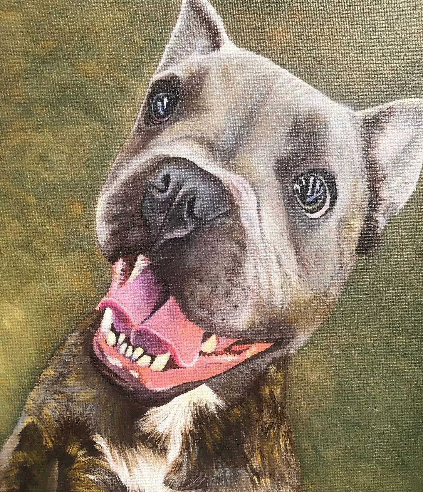 Close-up of a happy dog, possibly a pitbull, with its mouth open, tongue out, and wearing a pink collar, outdoors with green background.