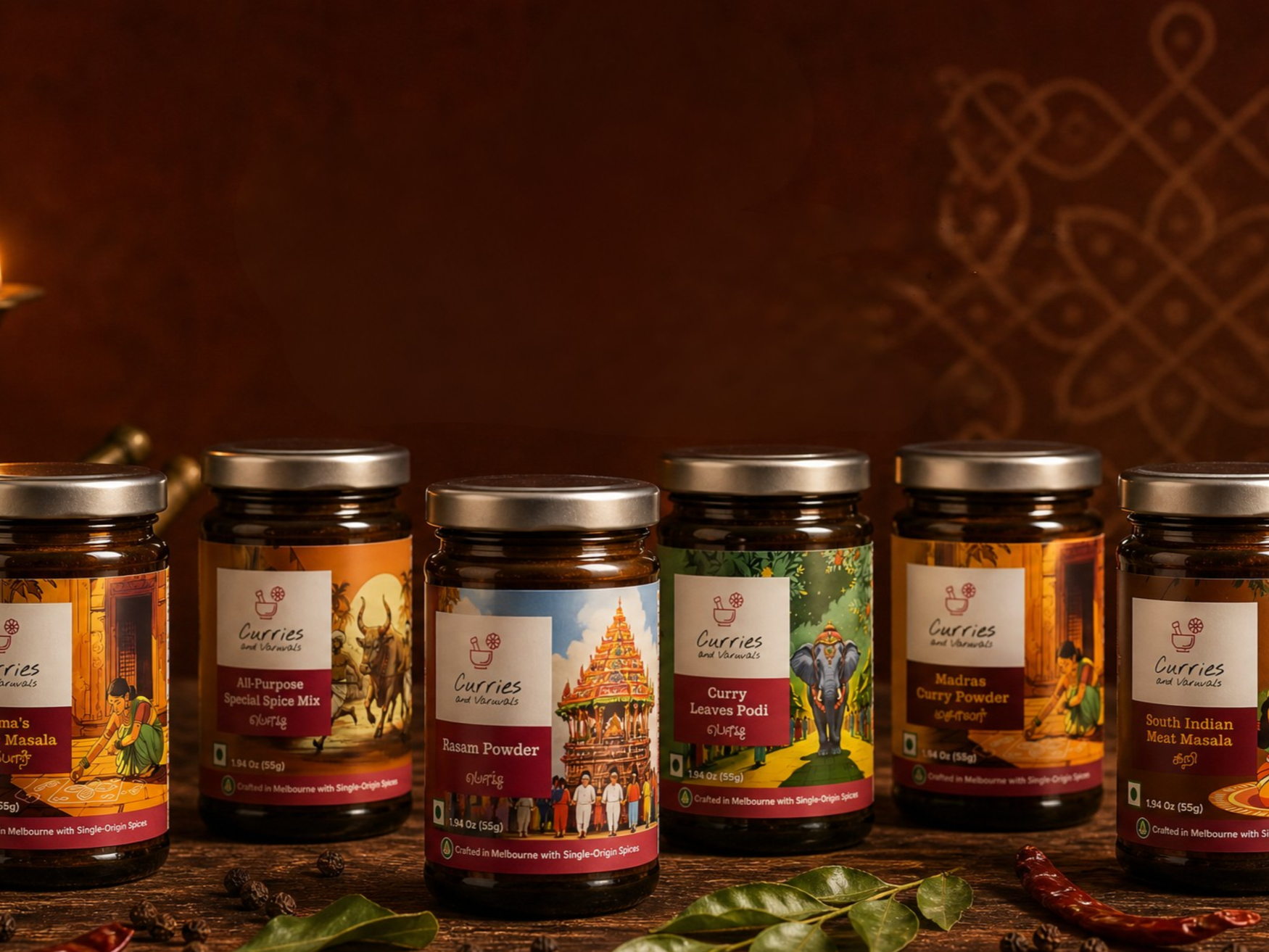 Six spice jars with colorful labels featuring Indian and Southeast Asian culture, placed on a wooden surface with spices and green leaves around.