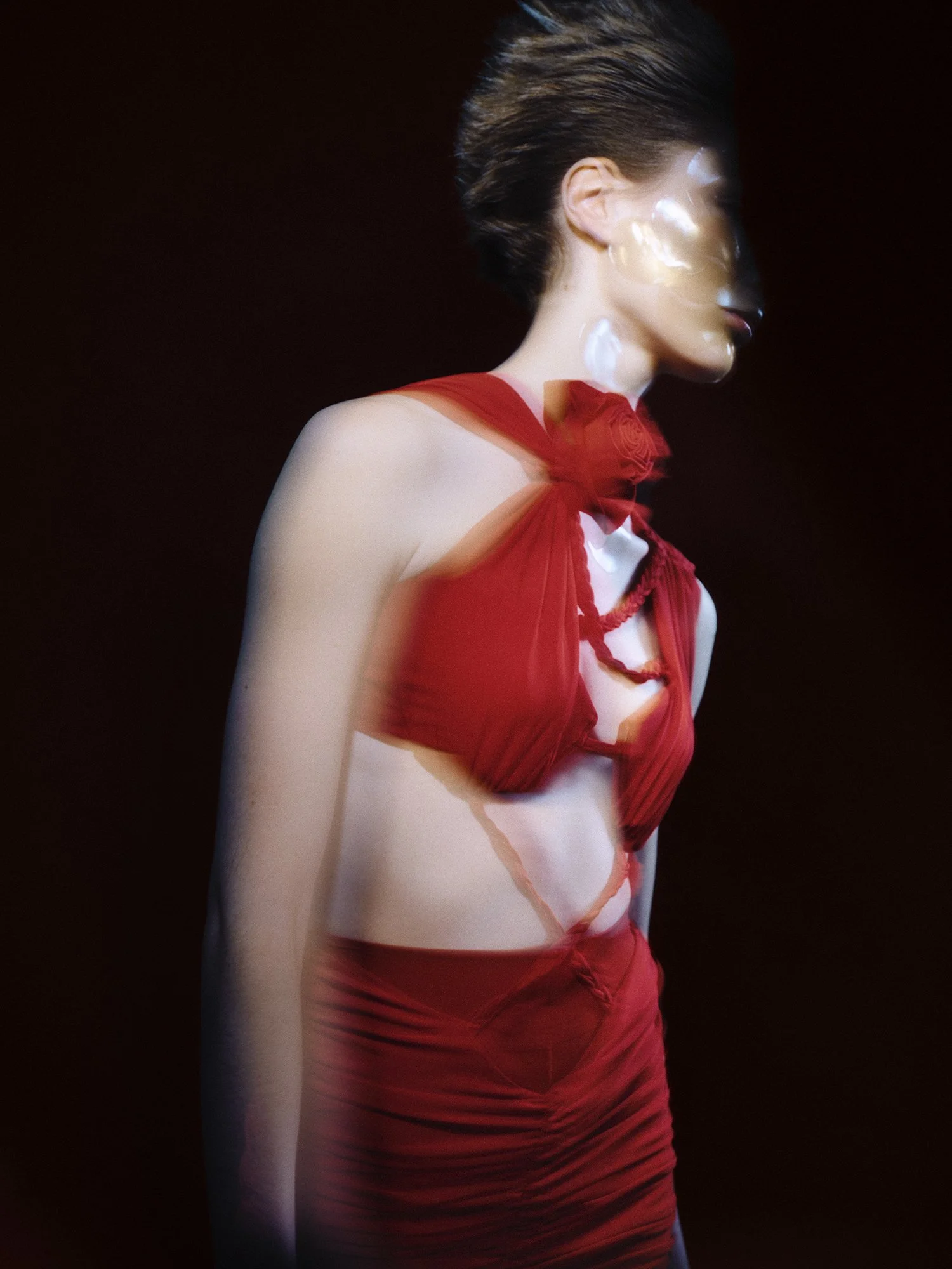 Mujer con cabello corto peinado hacia atrás, vestida con un vestido rojo y una bufanda del mismo color, en un fondo negro