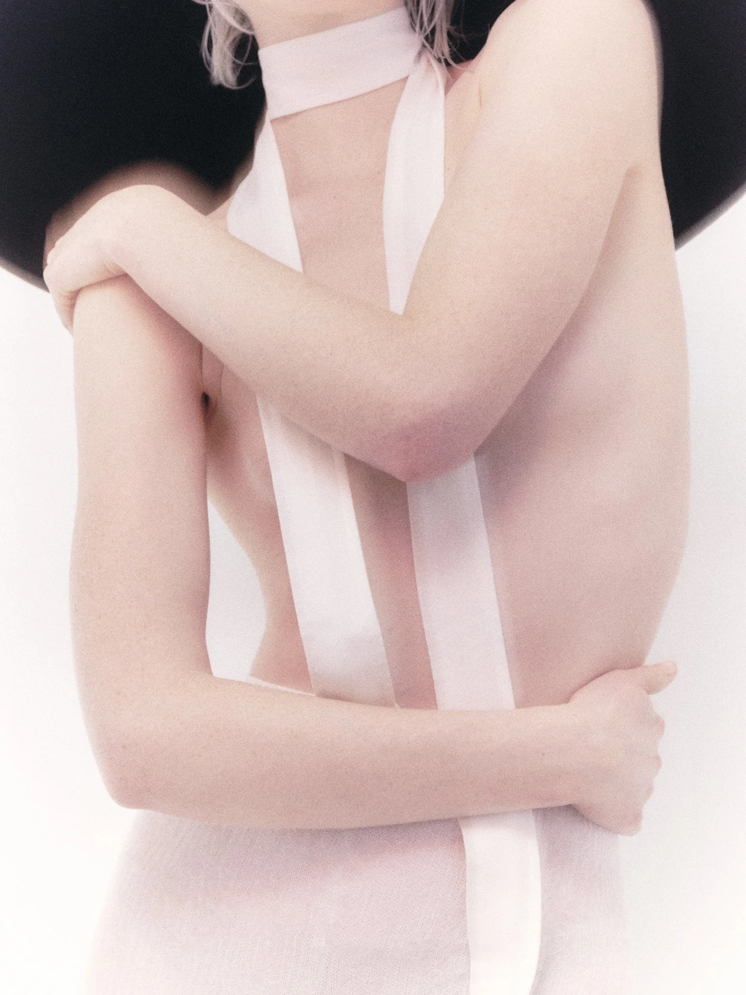 Mujer con una bufanda blanca y un sombrero negro, abrazando sus brazos.