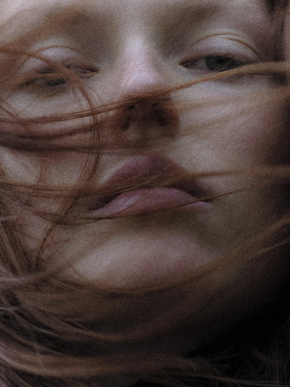 Primer plano de una cara con cabello mojado y caída, expresión neutra, ojos parcialmente cerrados, piel clara.