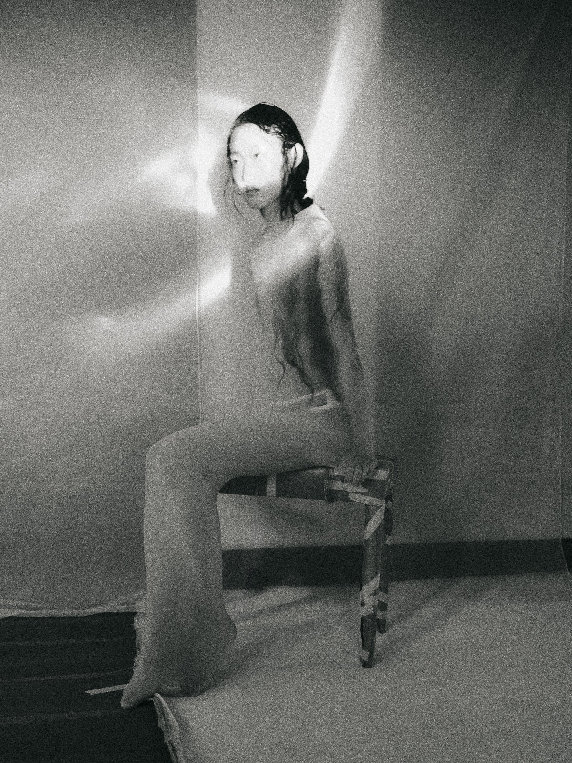 Mujer desnuda sentada en una silla en una habitación con iluminación tenue