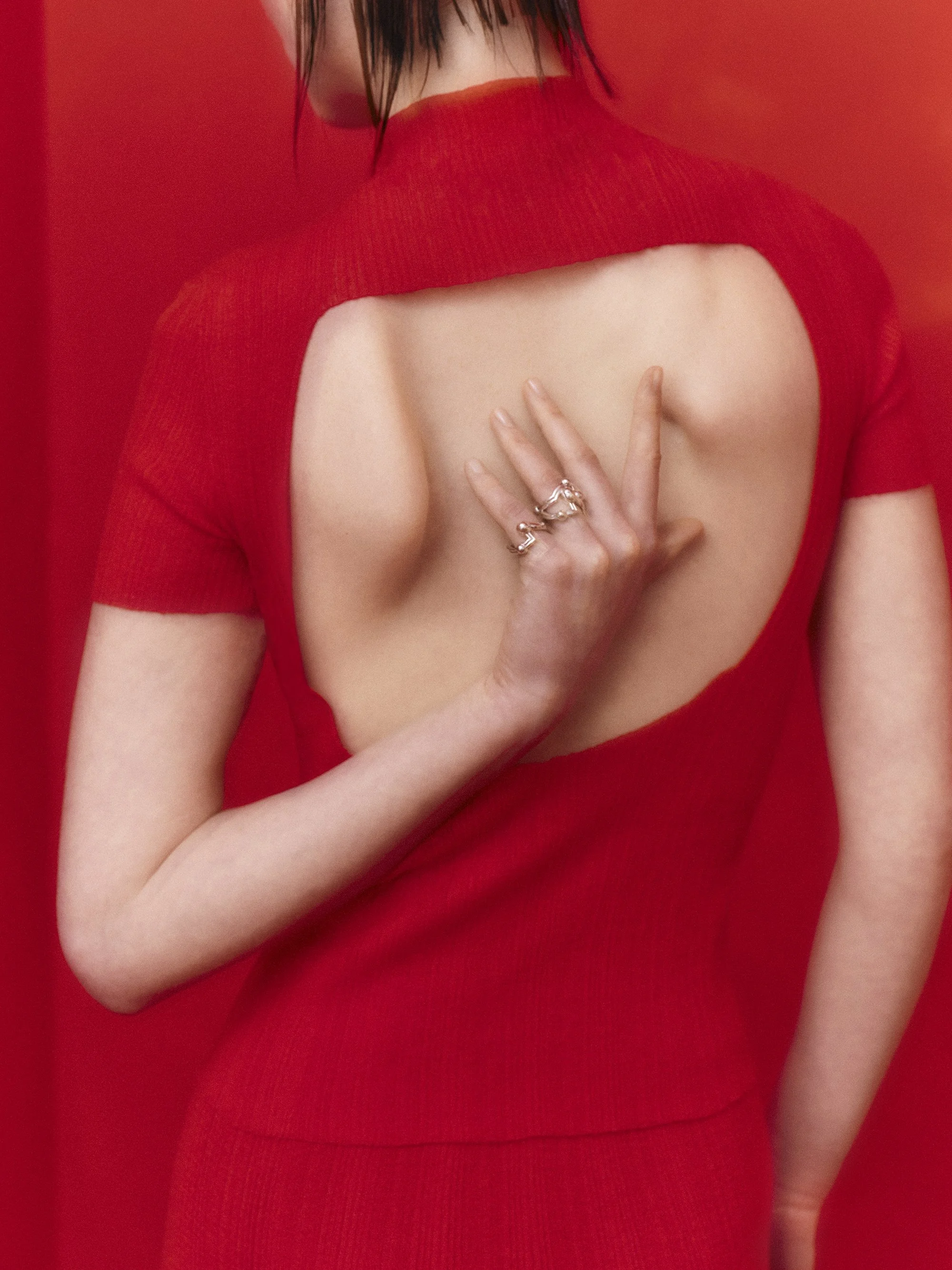 Mujer con vestido rojo con escote trasero, tocando su espalda, en un fondo también rojo.