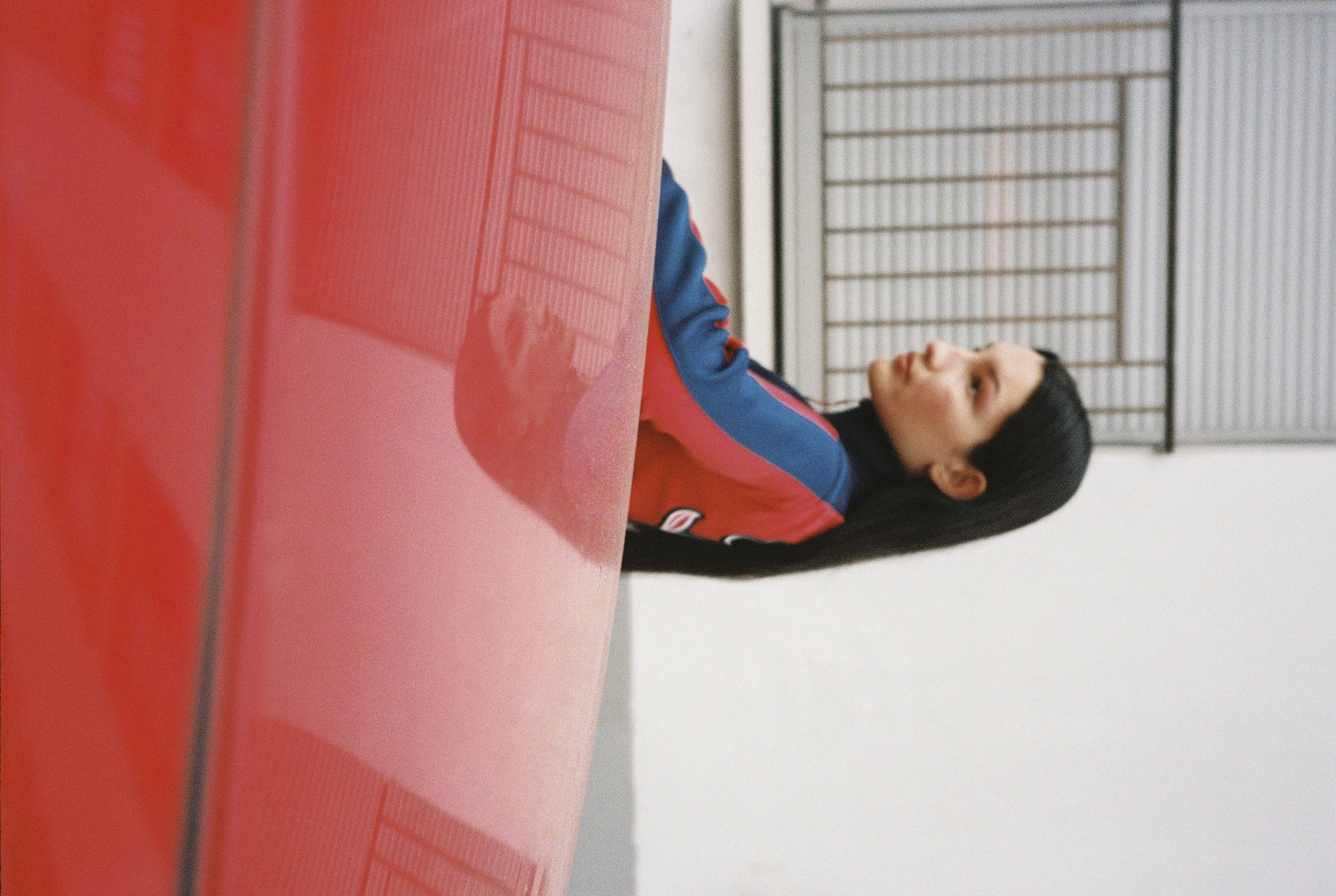 Una mujer con uniforme de ping pong sentada junto a una mesa de ping pong en una habitación con paredes blancas y una ventana de barrotes.