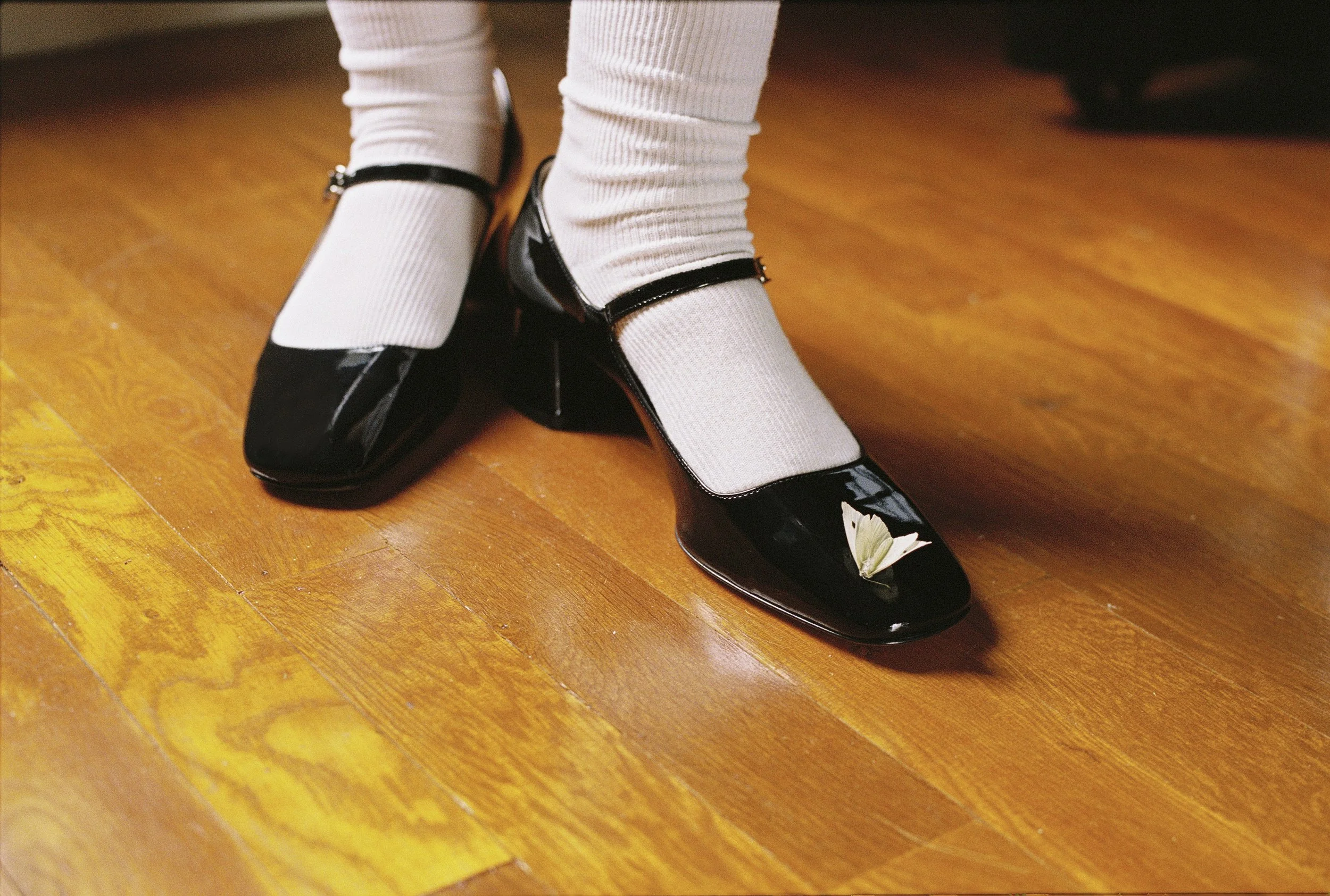 Zapatos de tacón negros con mariposas blancas y calcetas blancas con rayas negras sobre piso de madera.