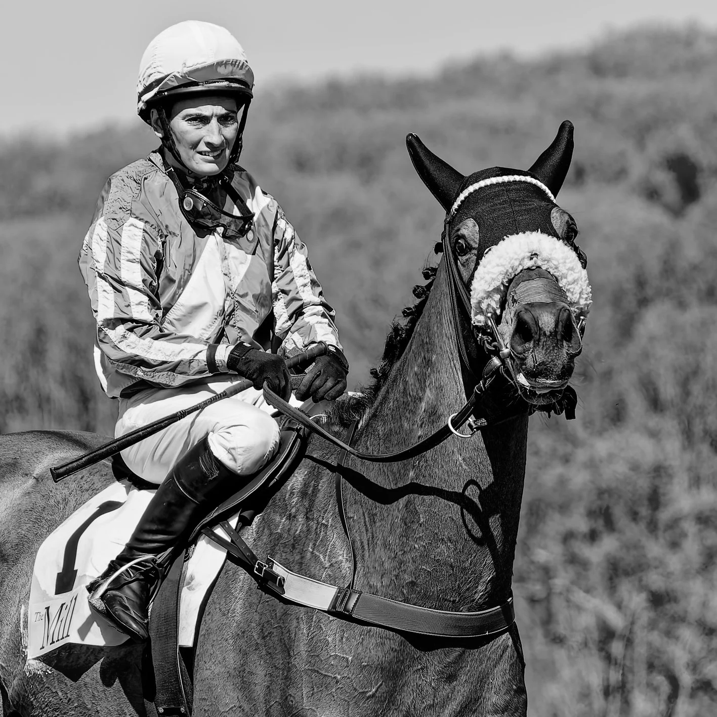 A woman dressed in equestrian riding attire, including a helmet, riding a decorated horse outdoors.