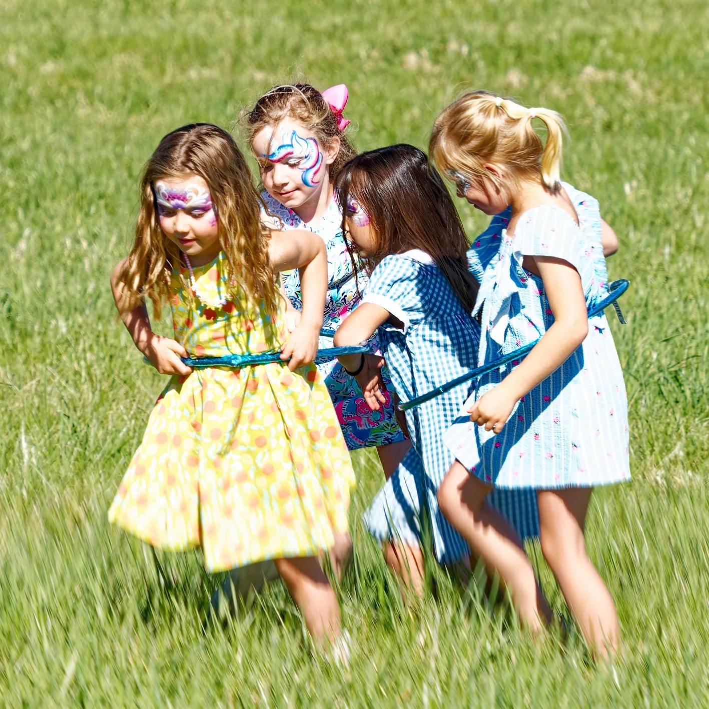 Five young girls with face paint engaged in a game of tug-of-war in a grassy field.