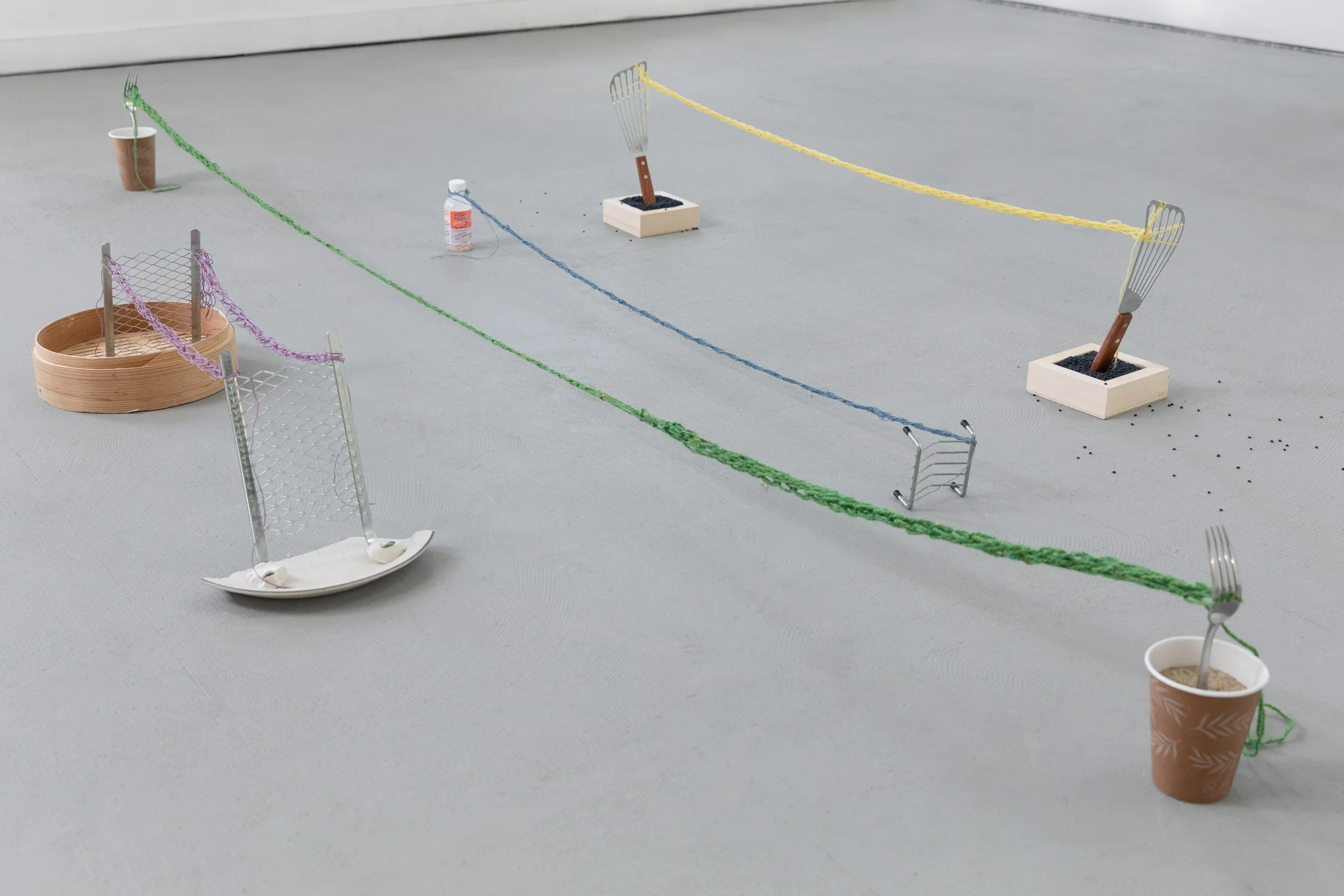 Miniature tennis court made with string, small metal tennis rackets, and paper cups as containers, set up on a flat surface for a tabletop game or display.