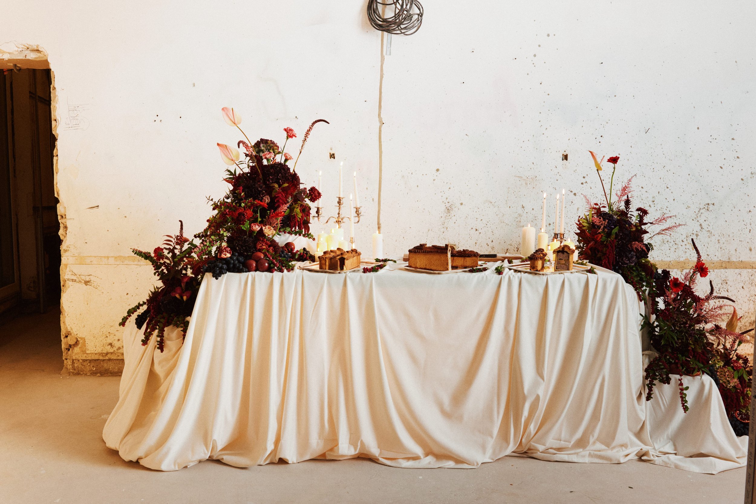 Tableaux décoratifs avec des fleurs rouges et roses, bougies, et desserts, dans un environnement en cours de rénovation, avec un mur en plâtre non fini.