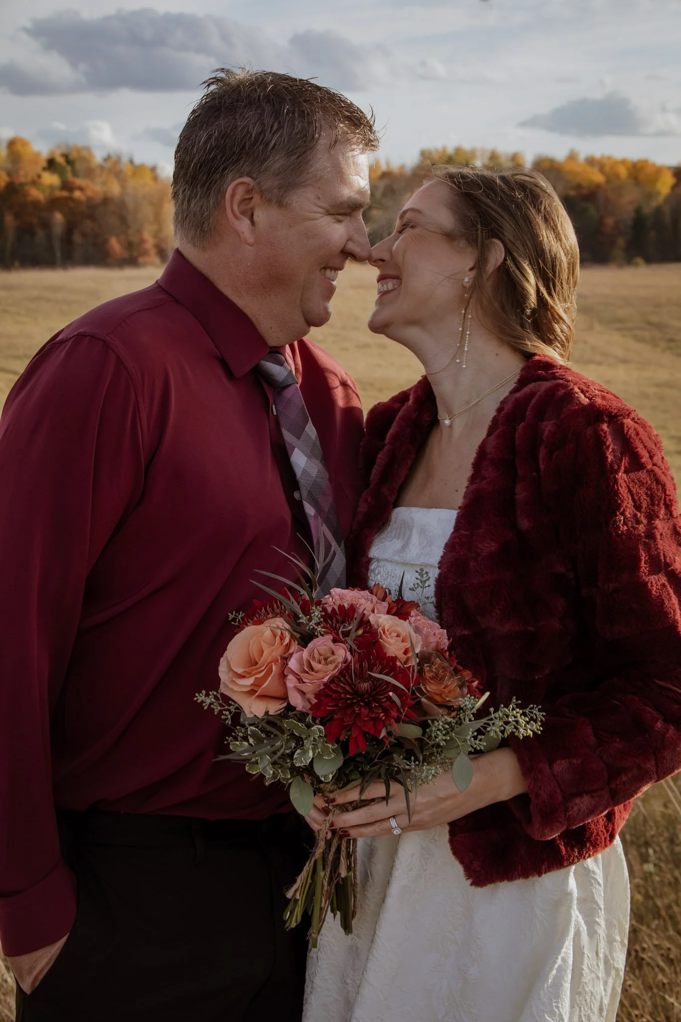 Black and white photograph of a bride and groom close-up, with the groom embracing the bride from behind, both smiling gently.