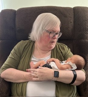 Older woman with gray hair and glasses holding a newborn baby.