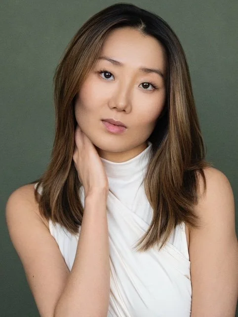 Portrait of an Asian woman with shoulder-length brown hair, wearing a white sleeveless top, with a green background.