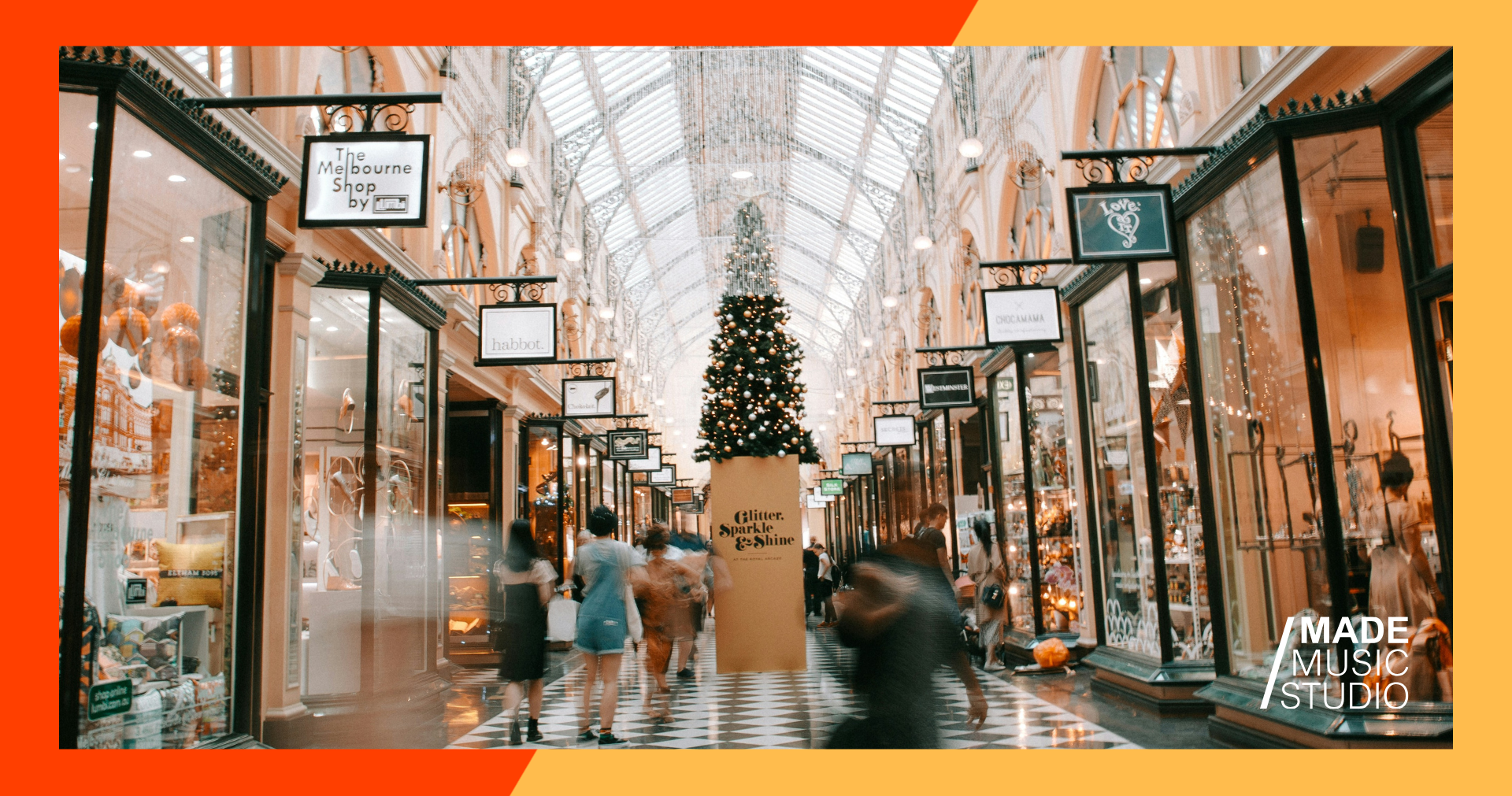 A walkway in a busy mall, decorated with string lights and a Christmas tree.