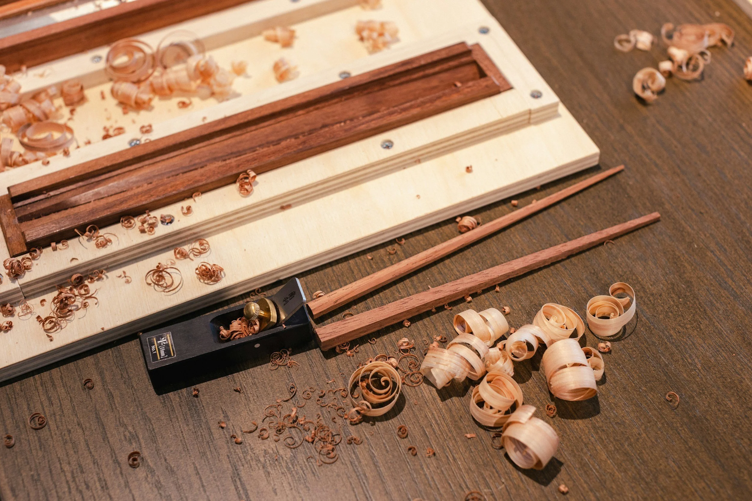 Wooden hand plane tool, wood shavings, and wooden planks on a workbench, used for woodworking.