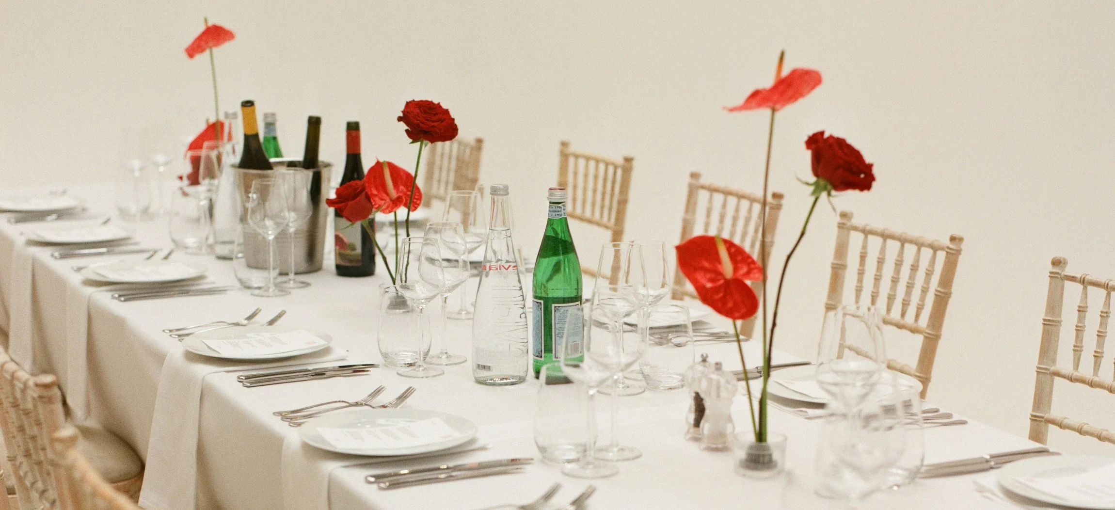 Modern wedding table with single-stem red roses and anthuriums in small glass bowls with kenzan placed along a white tablecloth.