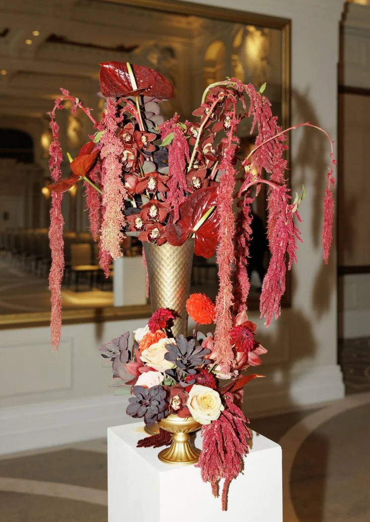 Tall burgundy wedding arrangement with anthuriums, amaranthus, orchids and roses on a pedestal.