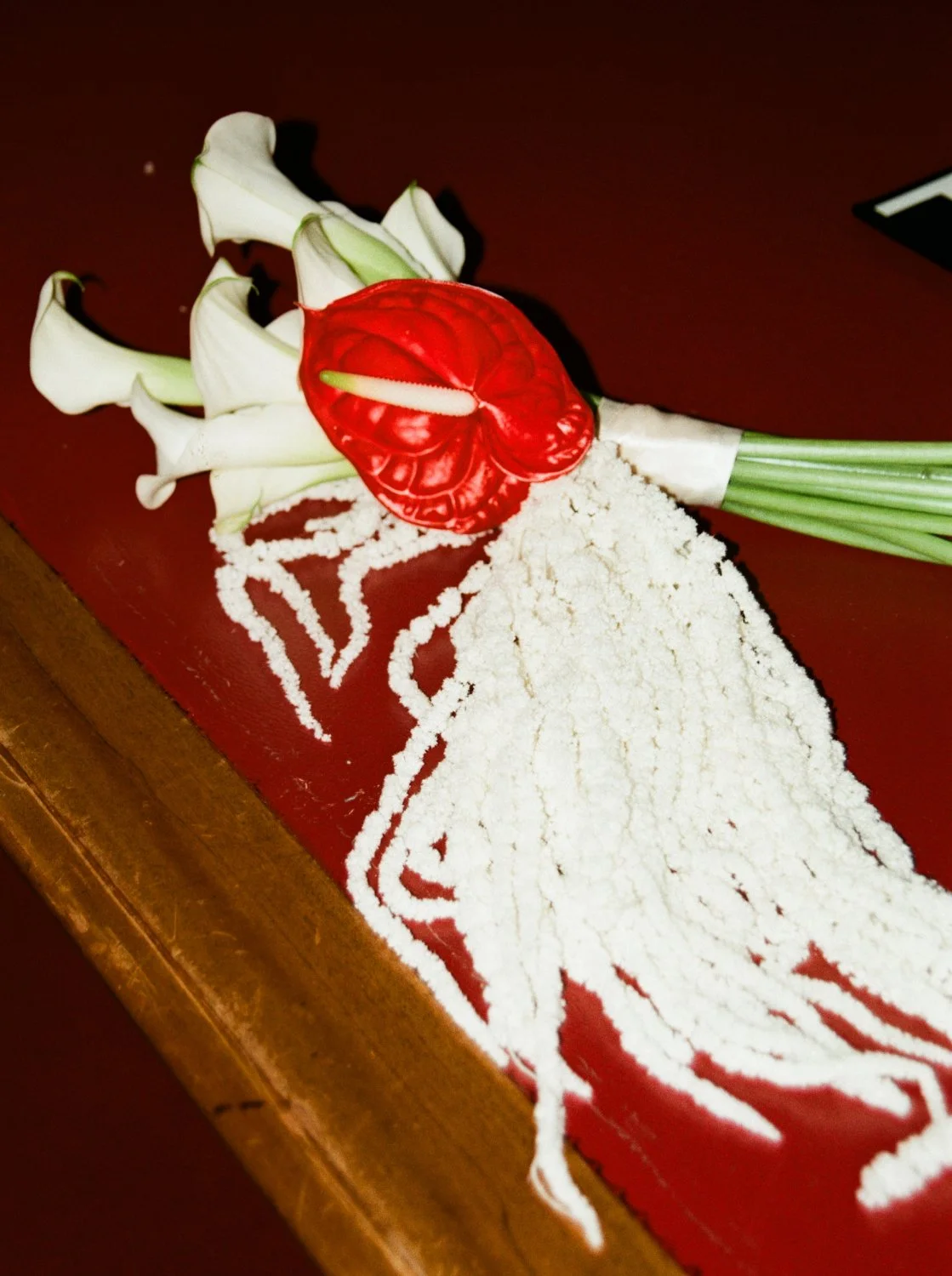 Modern bridal bouquet with white calla lilies, a red anthurium and long white amaranth resting on a table.