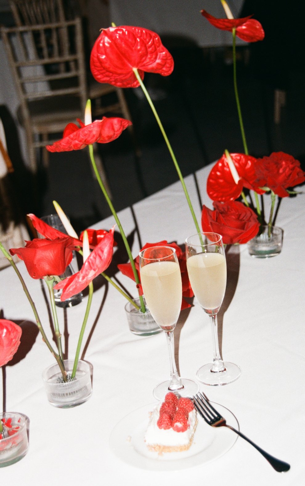 Wedding table styling with single-stem red roses and red anthuriums in small glass bowls with kenzan, beside dessert and drinks.
