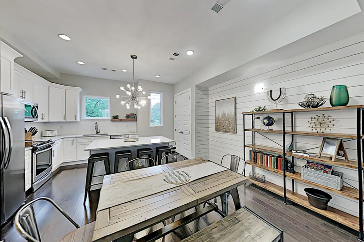 Kitchen and dining area in Music City Manor with a long wood table, island seating, and shelving on a shiplap wall