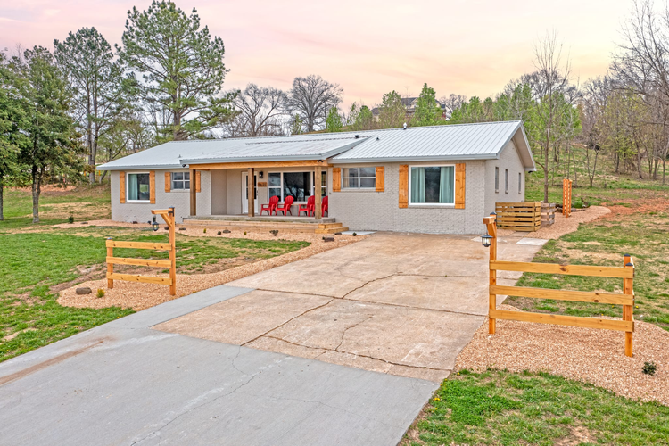 Single-story rental house with a metal roof, a covered front porch with red chairs, and a new concrete driveway, surrounded by trees