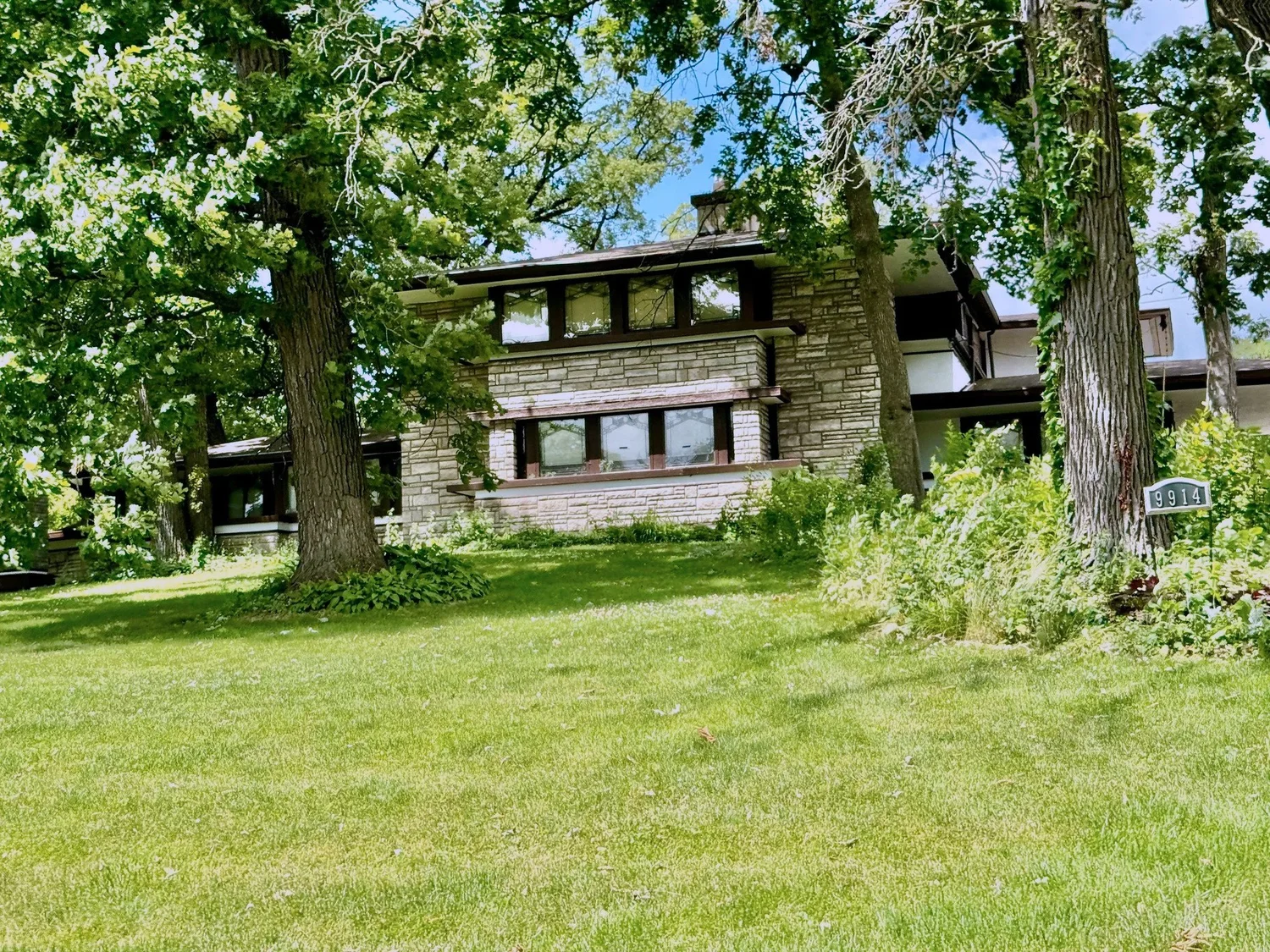 Prairie-style house with stone walls and a low hipped roof behind tall oak trees on Longwood Drive in Beverly