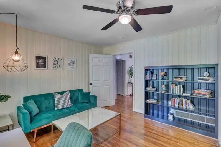 Living room with a teal velvet sofa, a glass coffee table, and built-in blue bookshelves