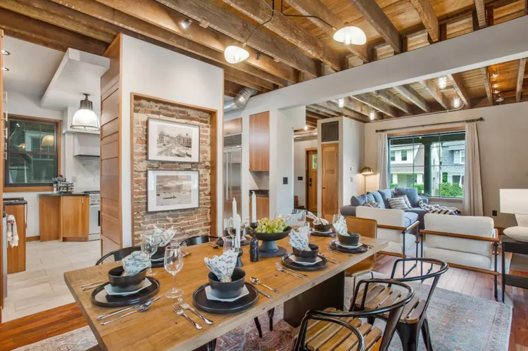 Dining table set for eight under exposed wood ceiling beams, open to the kitchen and living room