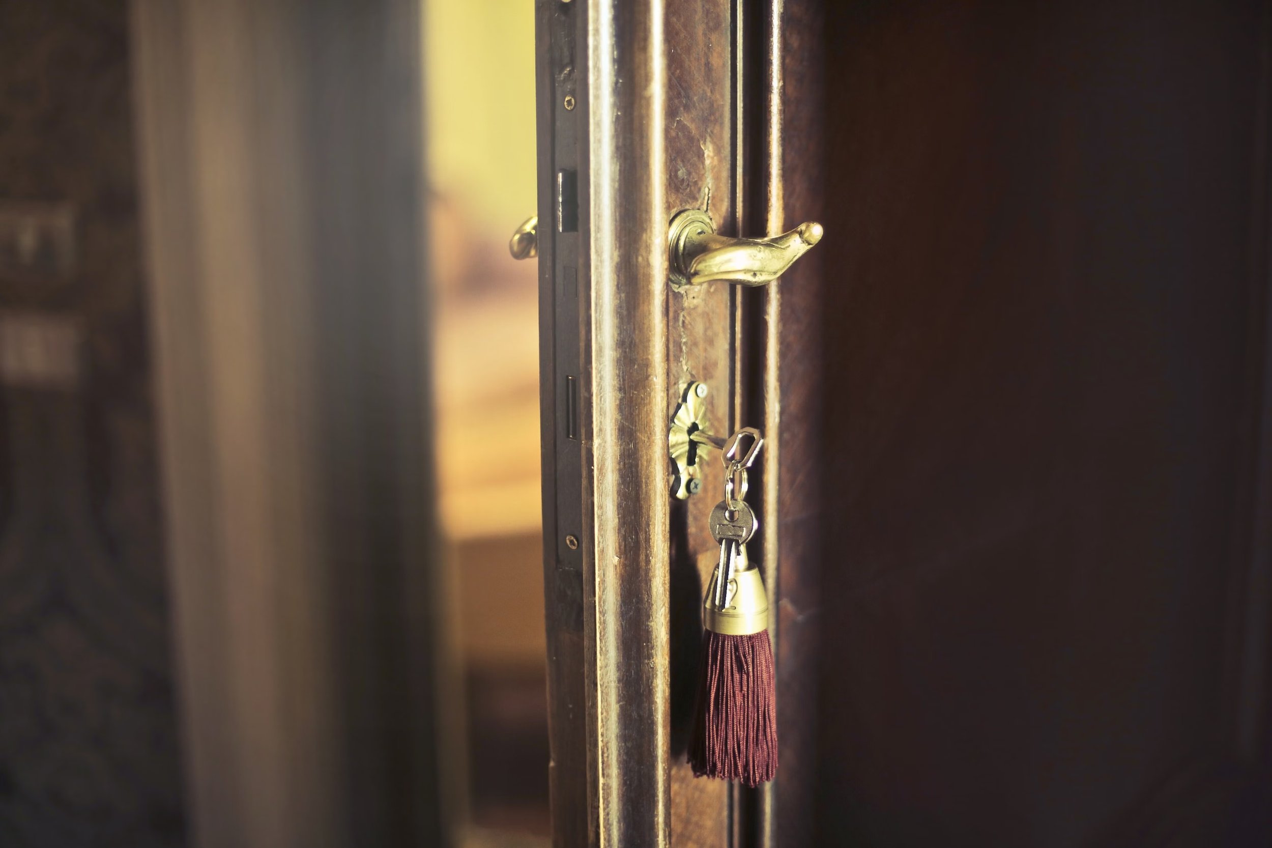 A house key with a red tassel hanging from the lock of an open wooden front door