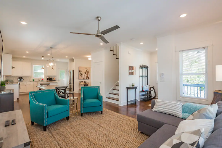 Open living room in Music City Muse with two teal armchairs, a gray sectional, and stairs to the second floor