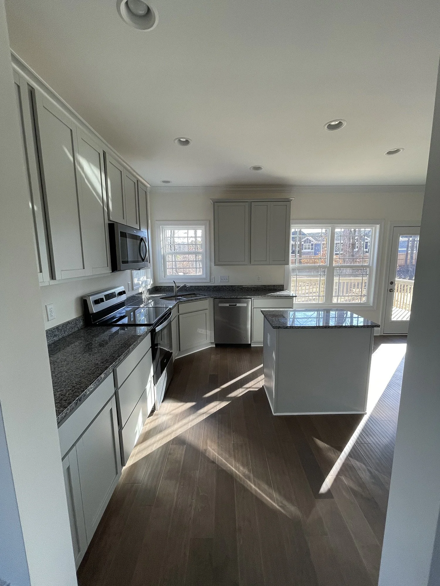 Kitchen with white cabinets, granite countertops, stainless steel appliances, a sink with a window above, and large windows letting in natural light.