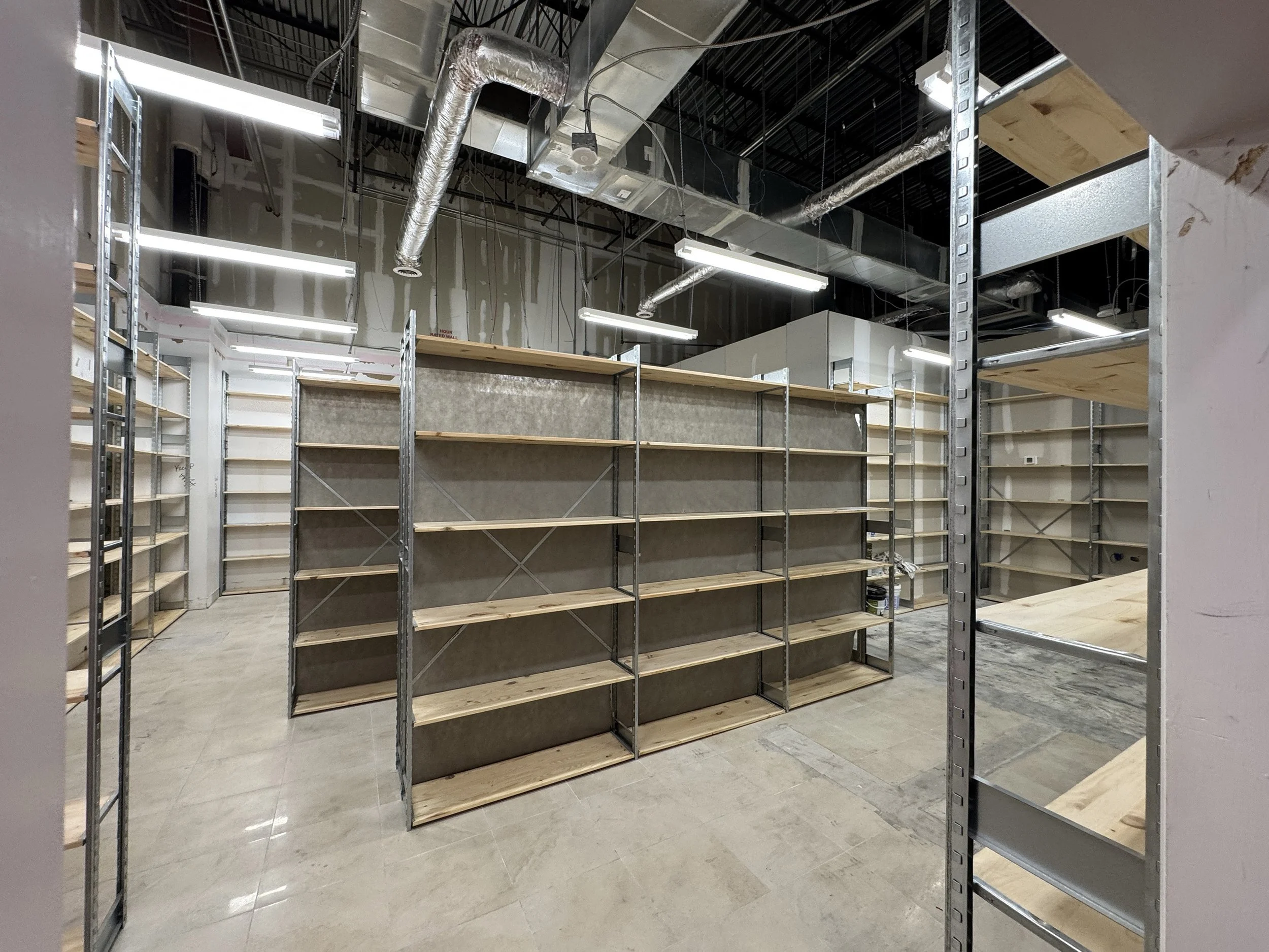 Empty retail store shelves with metal framing, some wooden planks, and exposed ductwork on the ceiling.