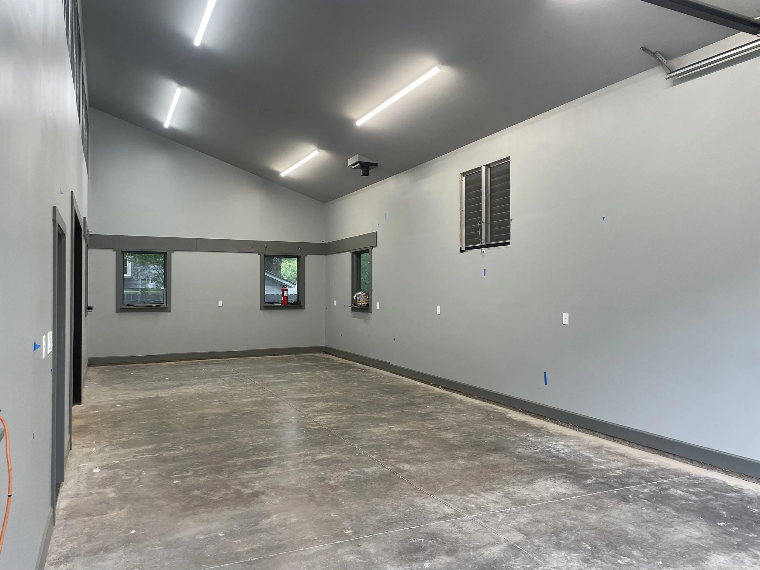 Empty room under construction with gray walls, exposed windows, fluorescent lighting, and unfinished flooring.