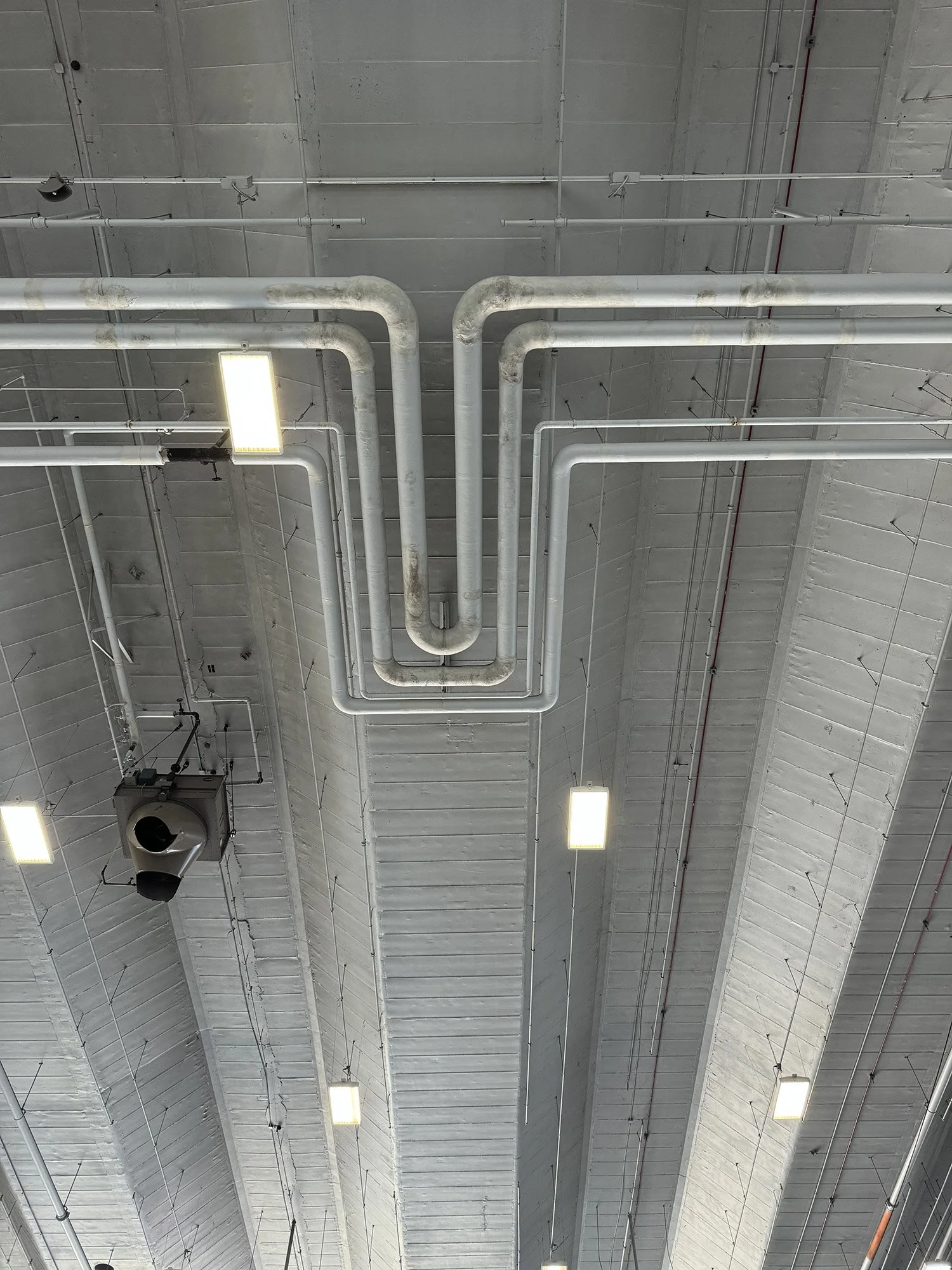 Ceiling with pipes, lights, and a ventilation duct in an industrial or commercial building.