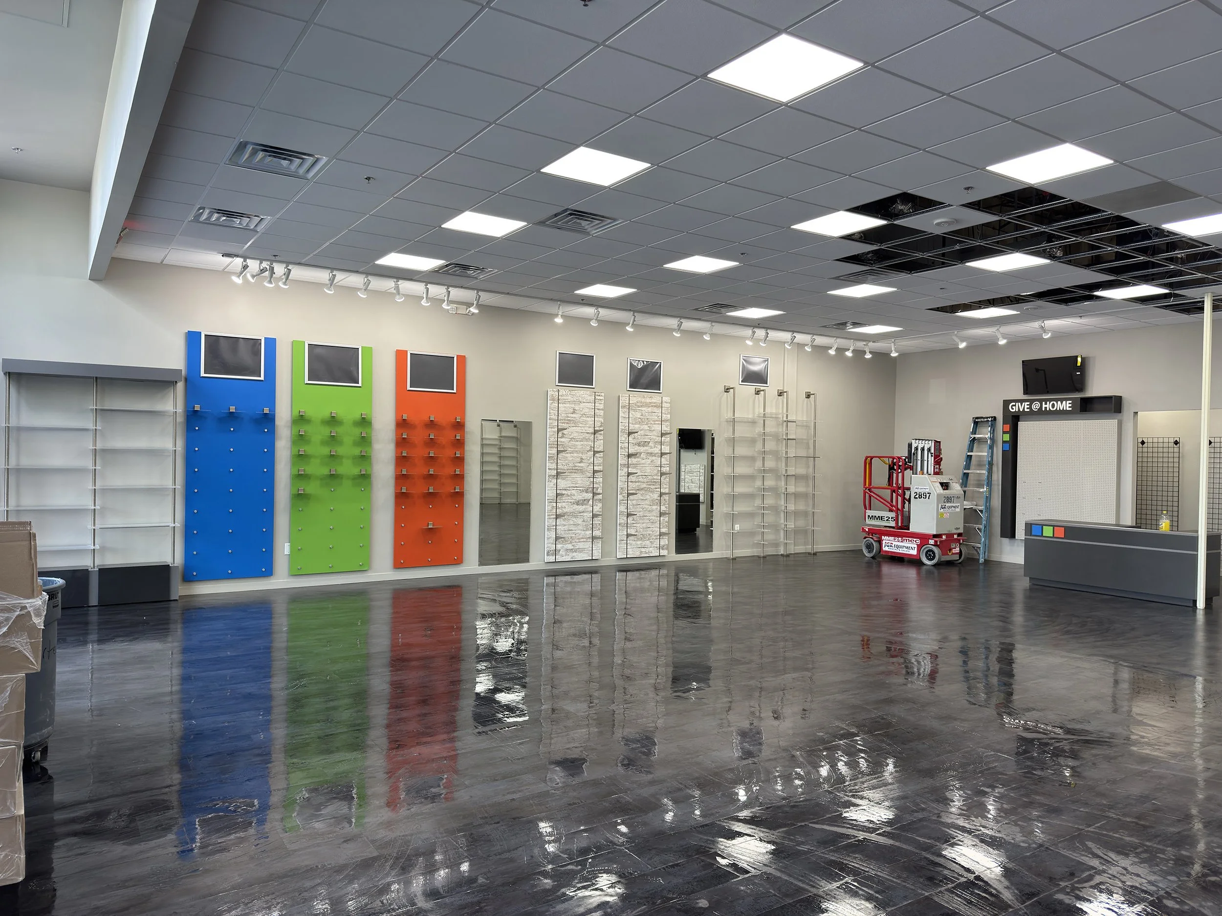 Store interior with empty shelves, colorful display boards, and a shiny reflective floor.