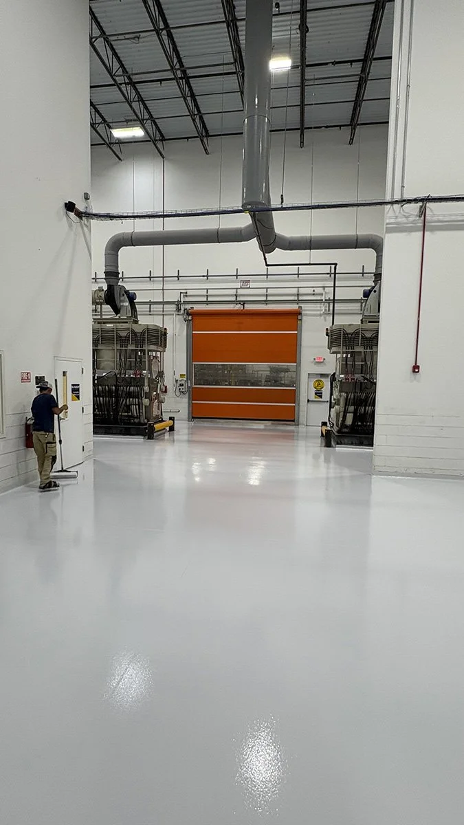 Large industrial warehouse with high ceilings, orange rolling door, and two HVAC units. A worker is operating a control panel on the left side.