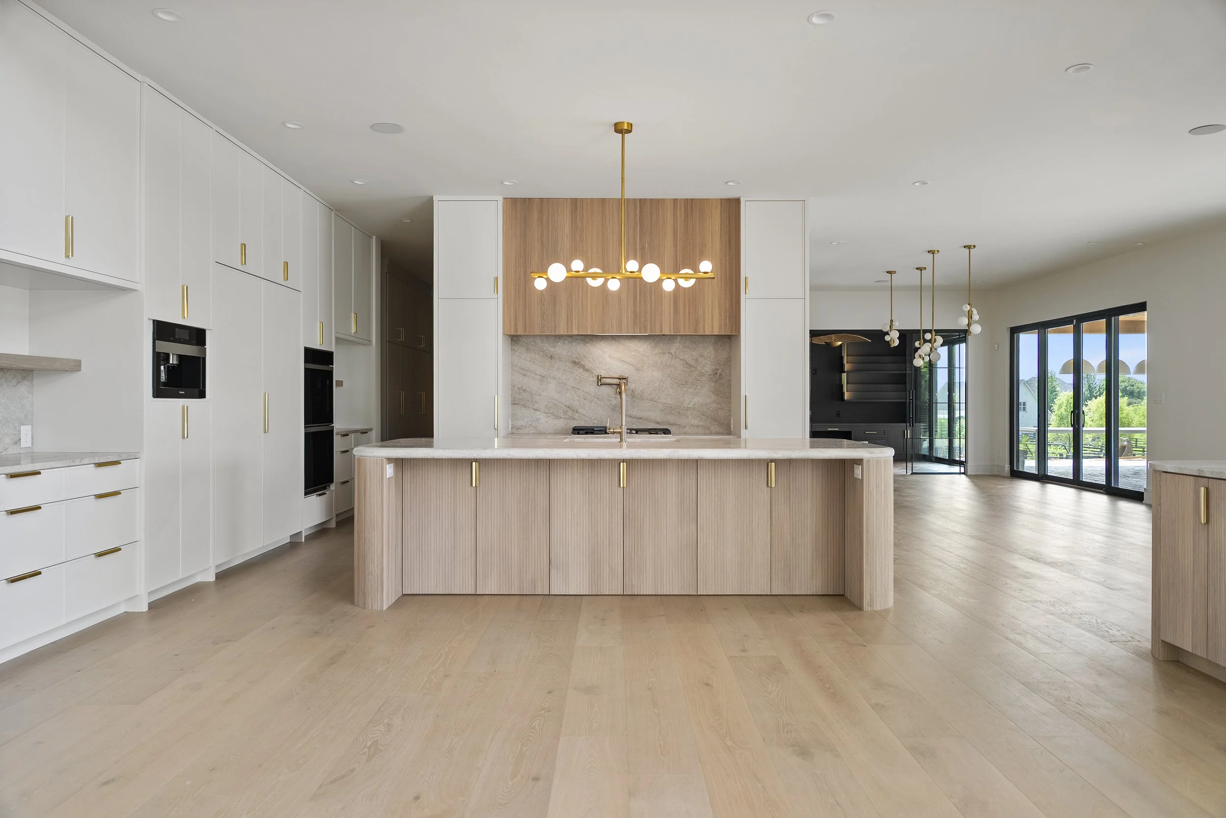 Bedroom with large arched window, stone accent wall, canopy bed, beige armchairs, and a round table. A decorative sculpture and vase are on the table, overlooking a scenic outdoor view.