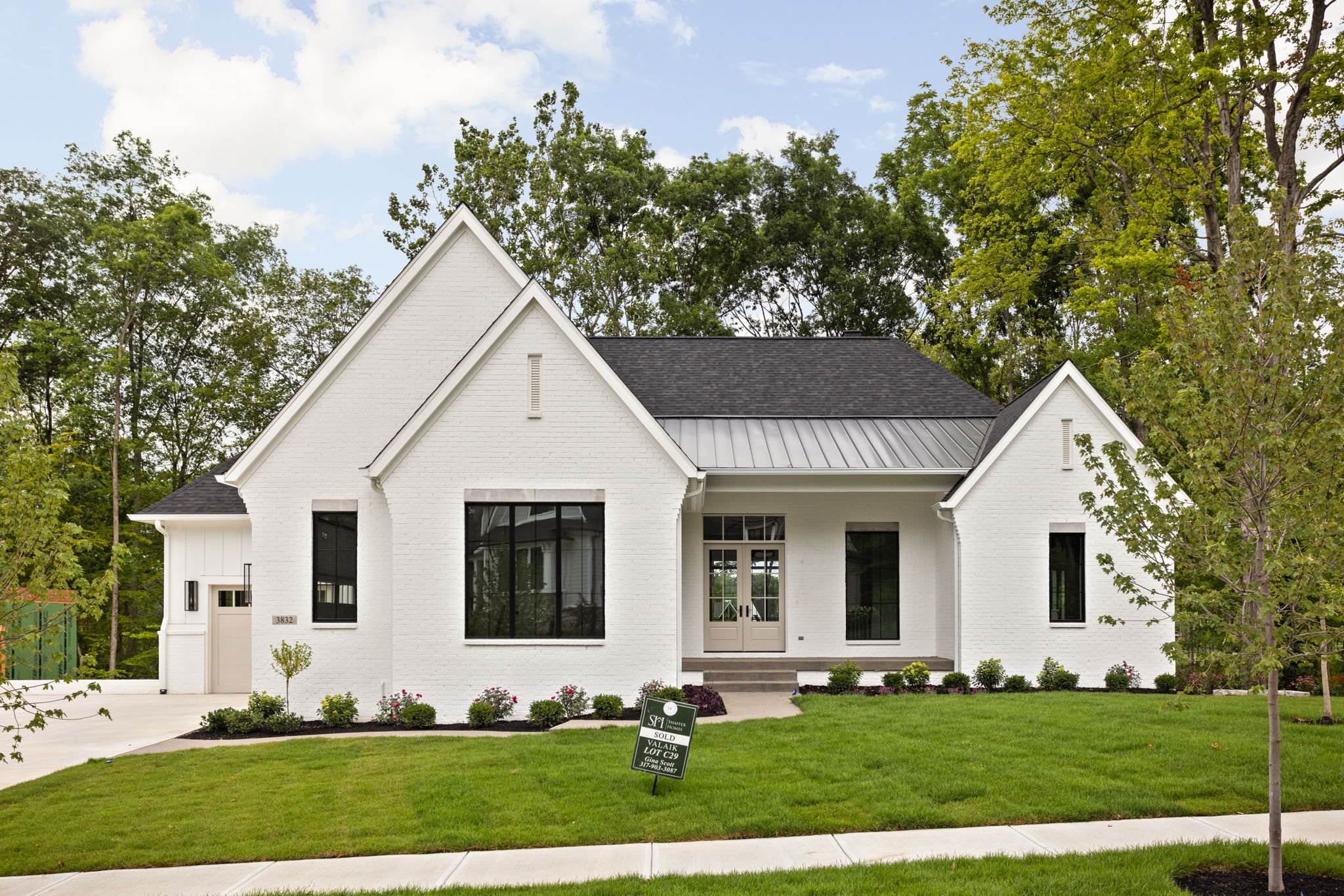 Modern white brick house with dark roof, surrounded by green lawn and trees, with a 'Sold' sign in the yard.