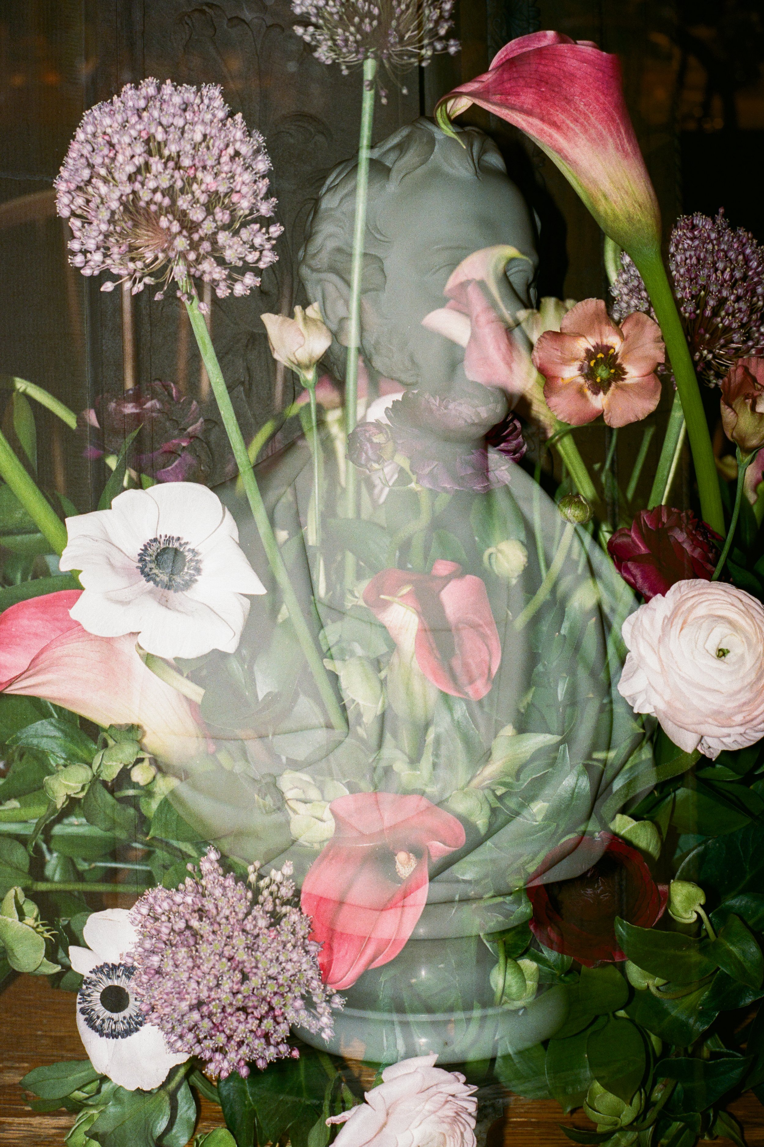 A reflection of a classical sculpture of a woman surrounded by a variety of colorful flowers.
