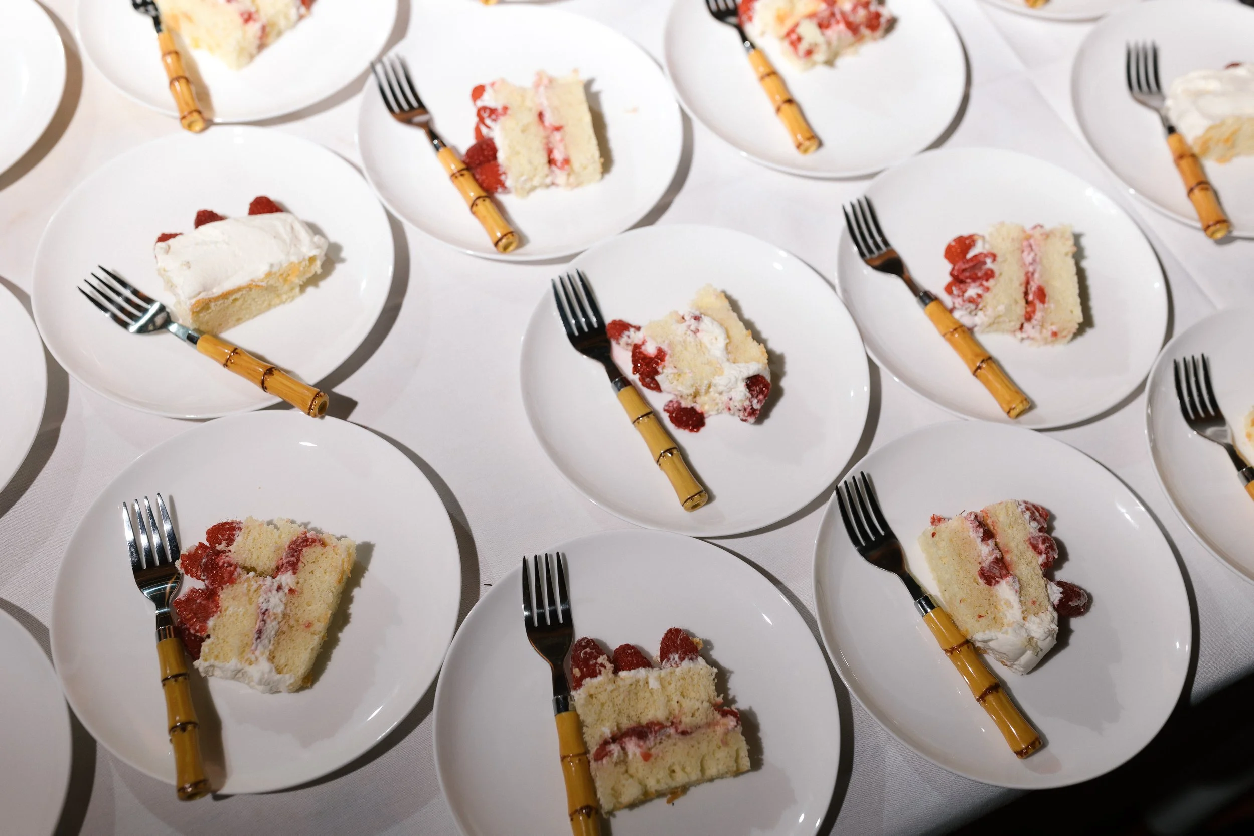 Several white plates with slices of strawberry shortcake and small forks with bamboo handles on a white tablecloth.