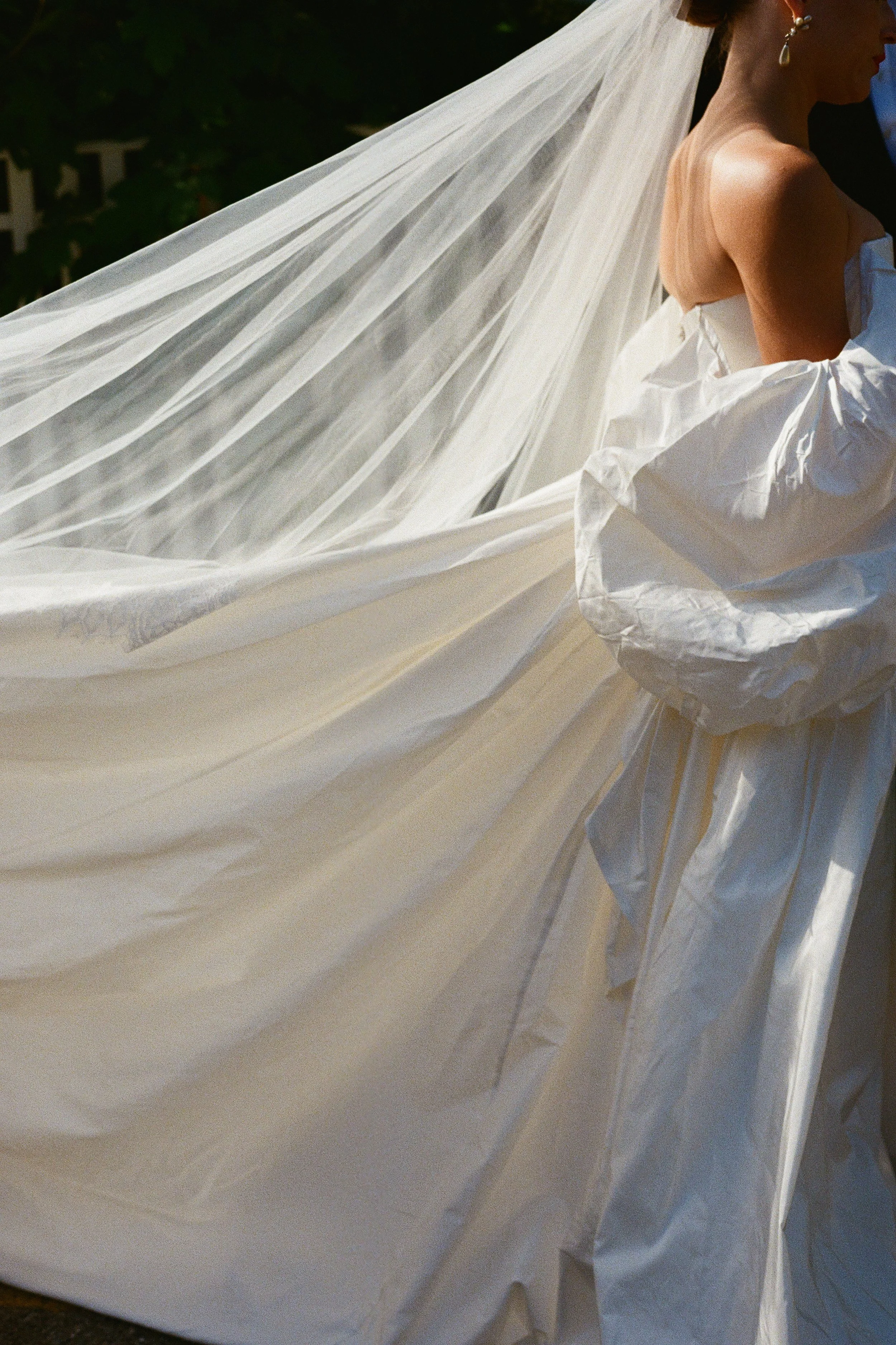 Close-up of a bride with an elegant wedding dress and long flowing veil, holding the fabric of her gown.