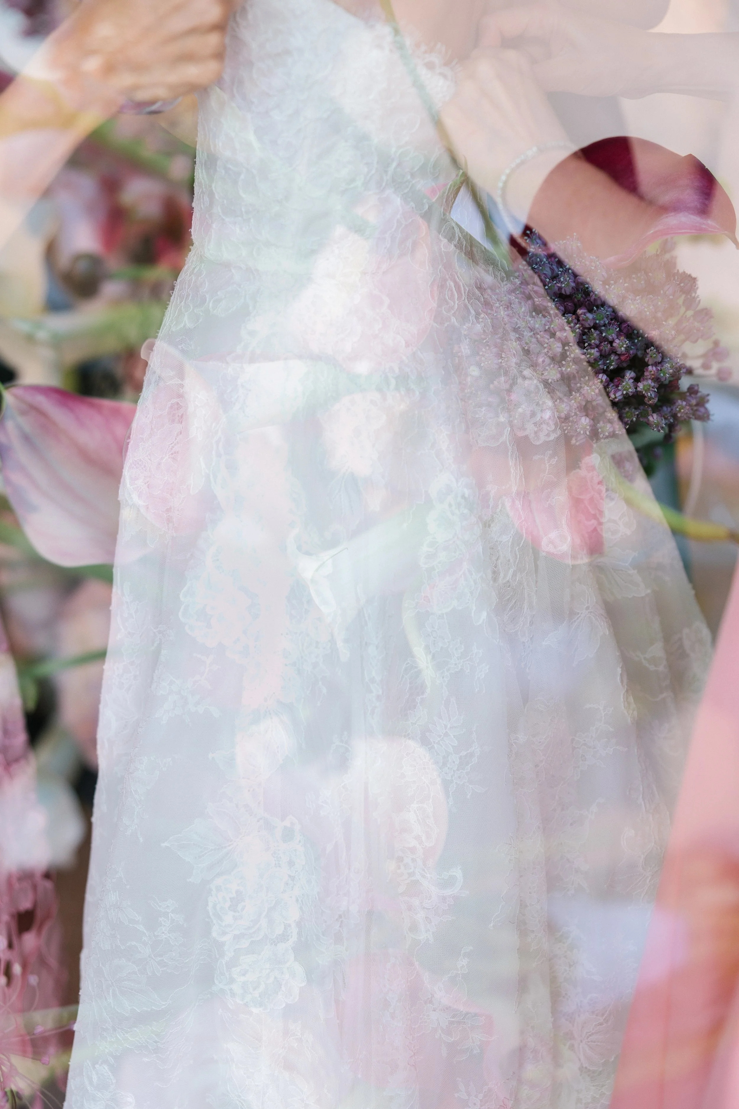 A wedding dress with lace details, partially transparent, overlaying a bouquet of purple flowers.