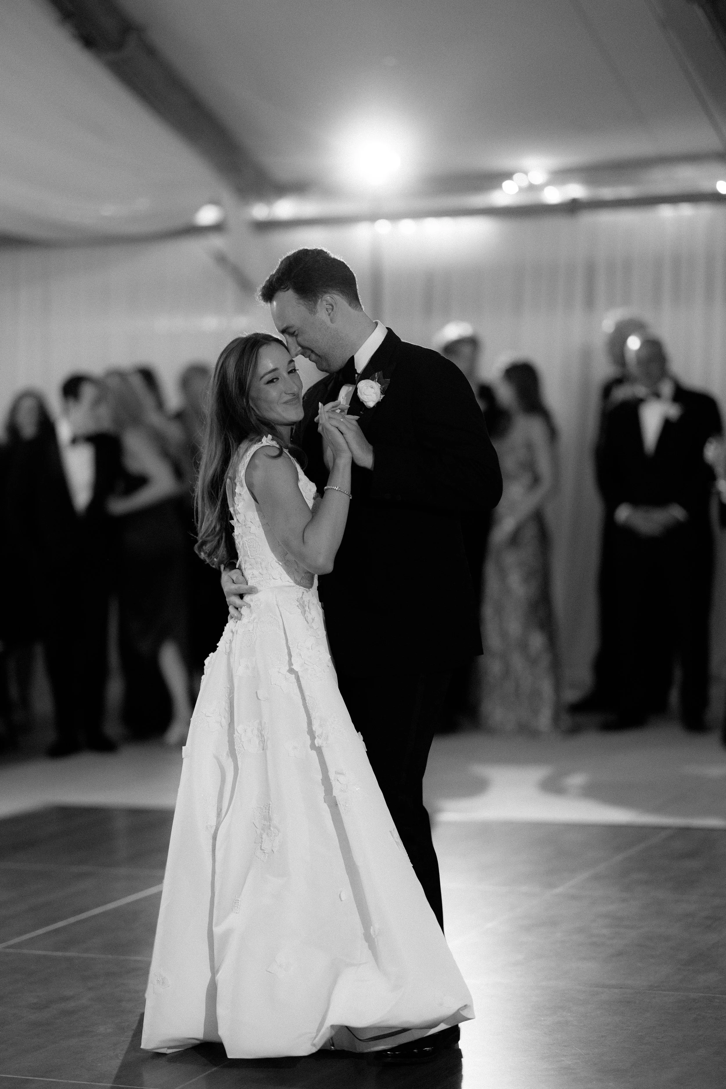 A bride and groom share a dance at their wedding reception, surrounded by guests in formal attire.