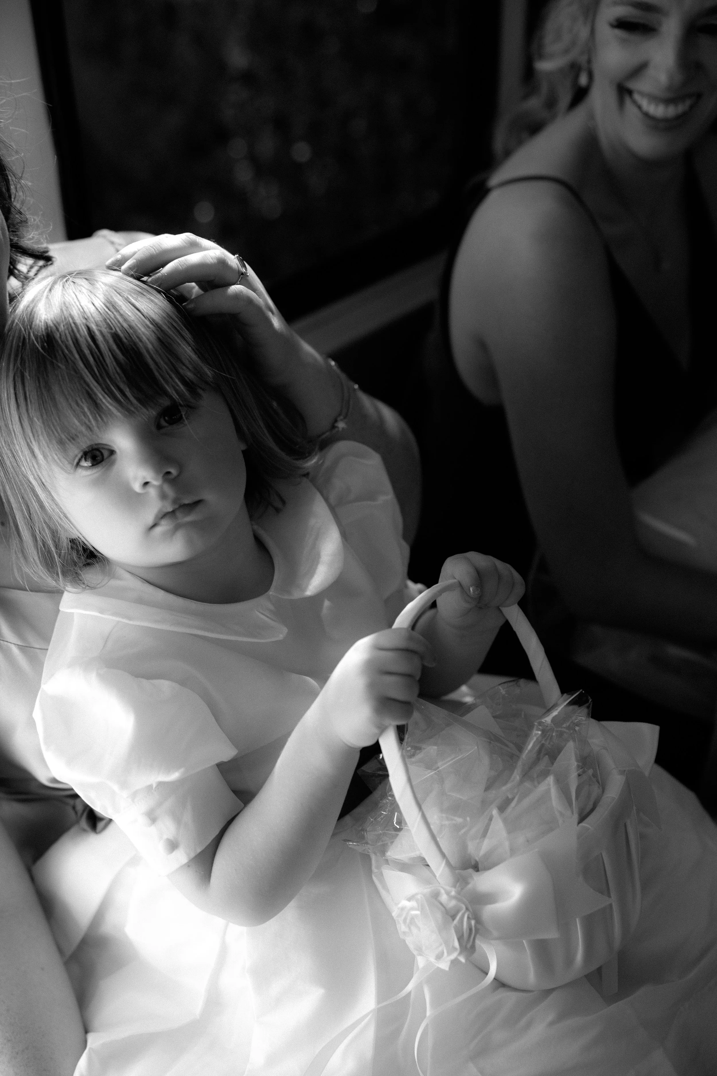 A young girl with medium-length hair holding a basket with a ribbon, sitting next to a smiling woman in a sleeveless top.