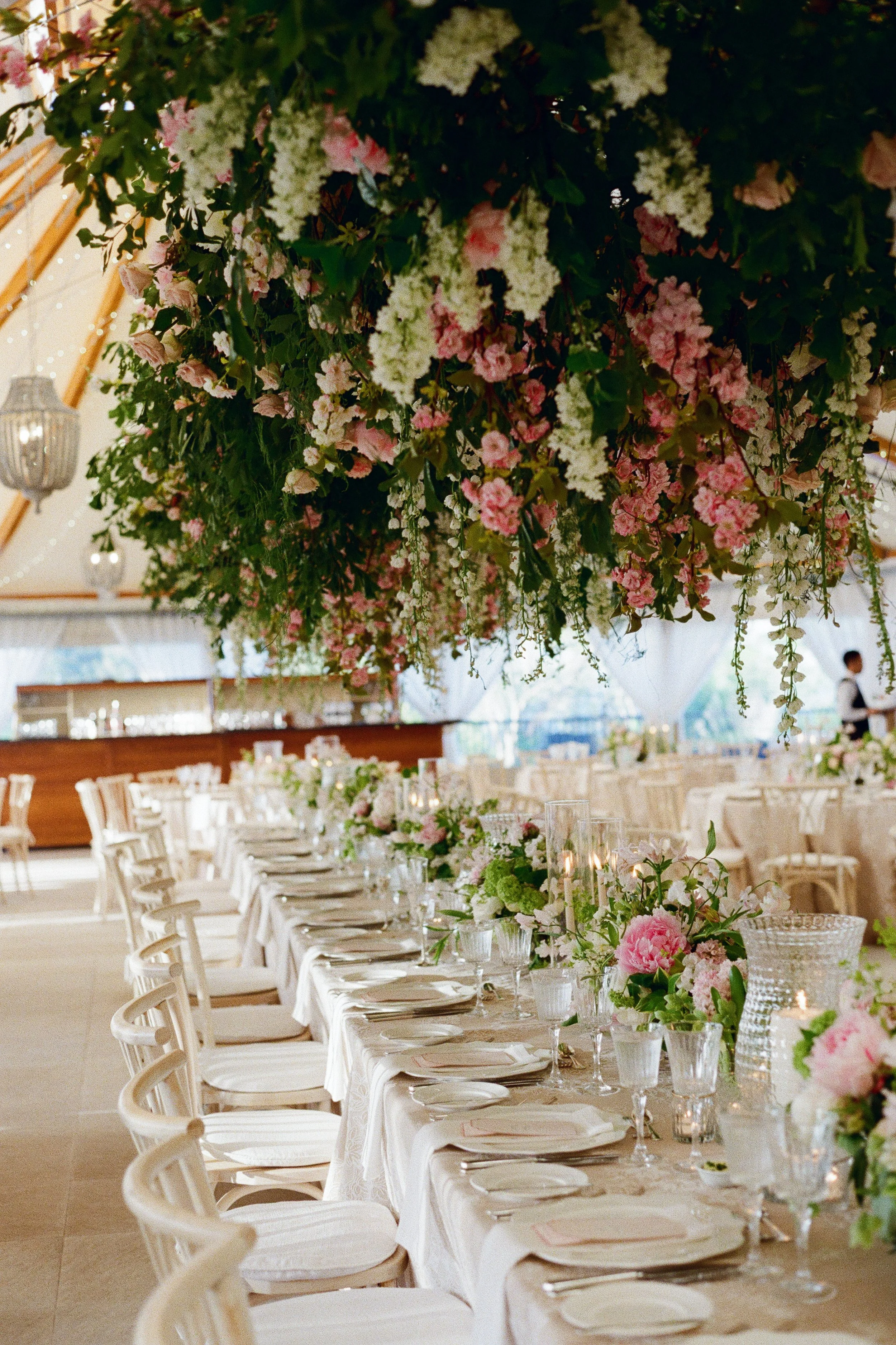 Elegant wedding reception table decorated with floral arrangements and hanging greenery in a tented venue.