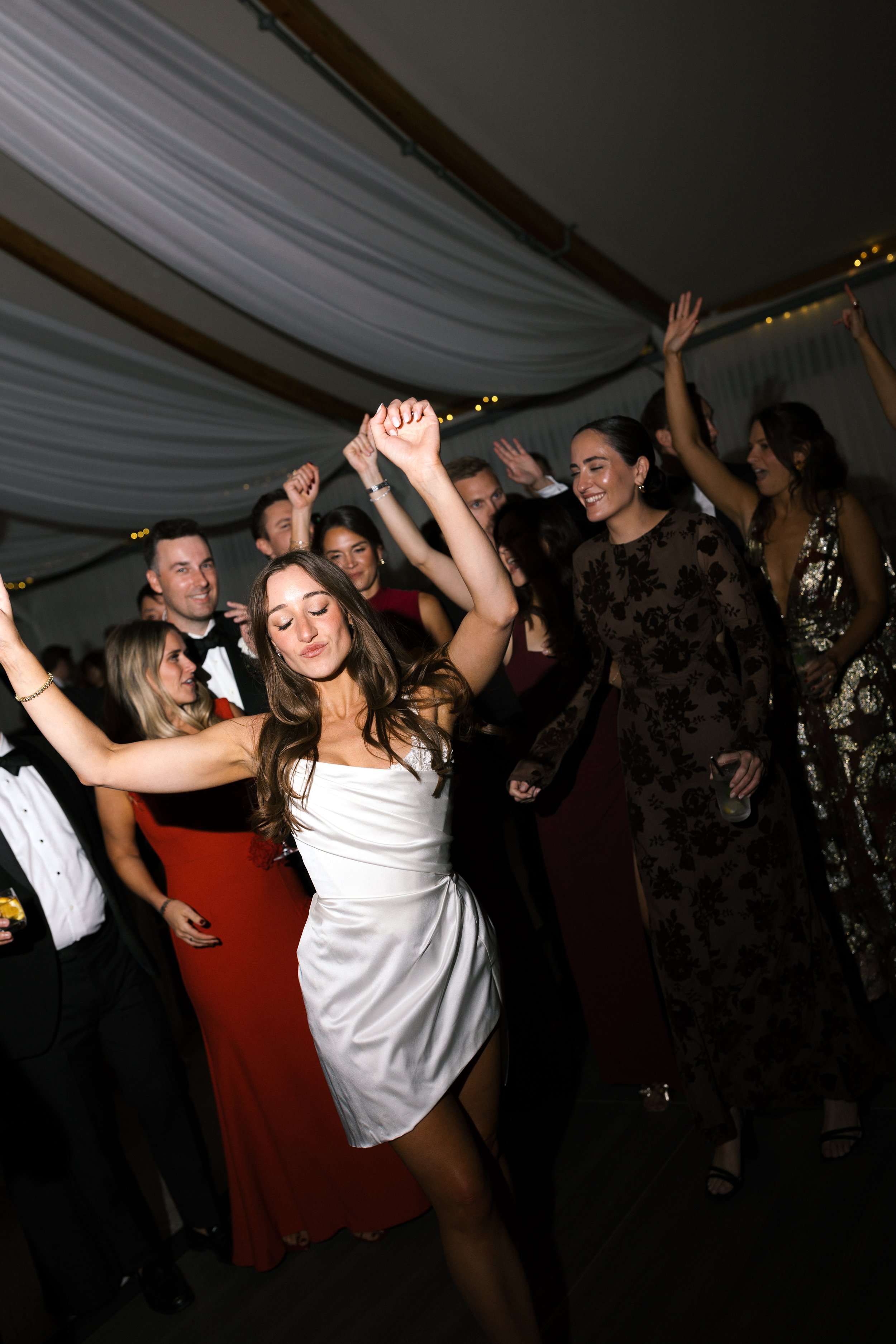 People dancing and celebrating at a formal event or party, with women in elegant dresses and men in tuxedos.