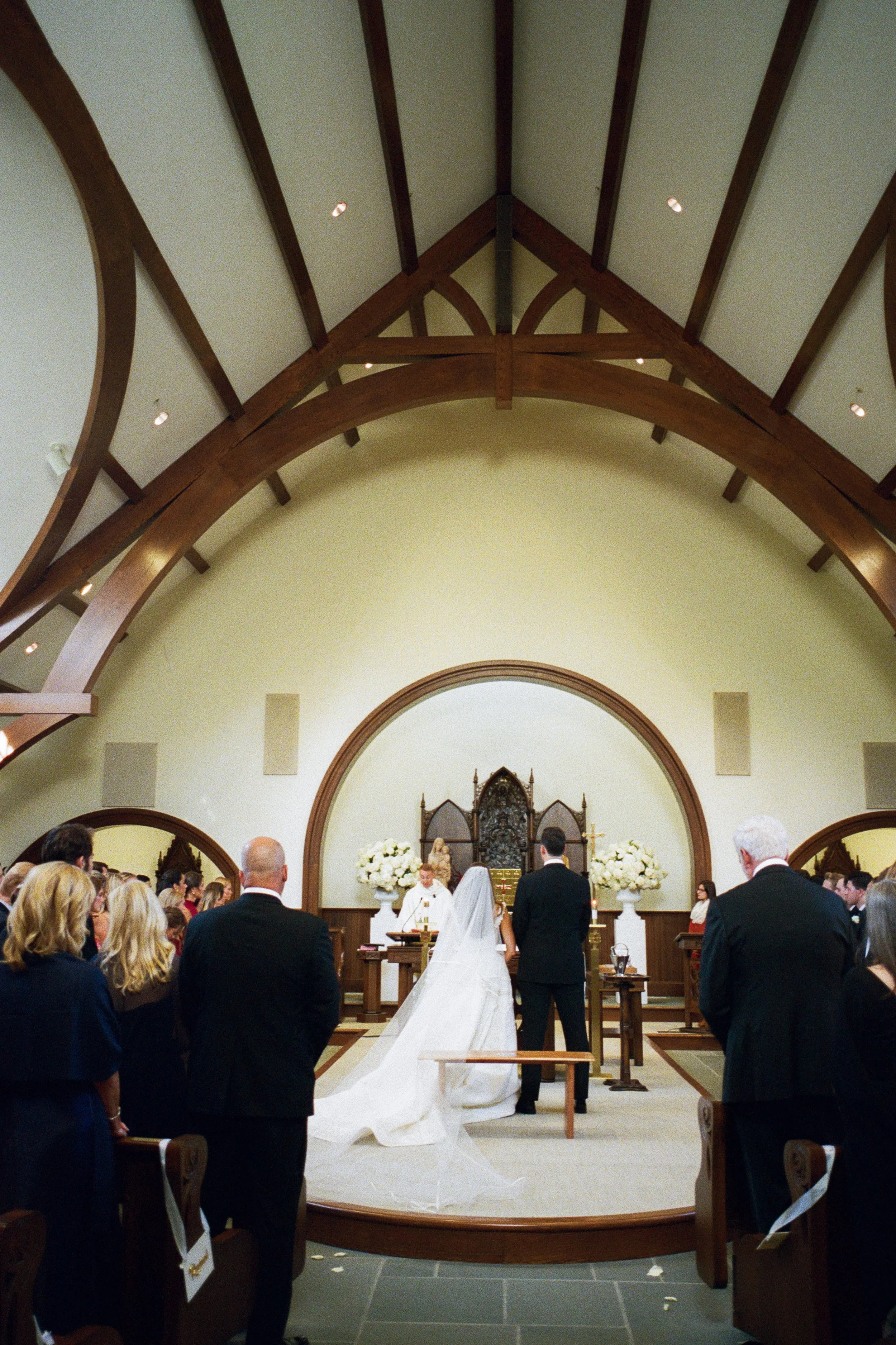 A wedding ceremony taking place inside a church with a bride and groom standing facing the altar.