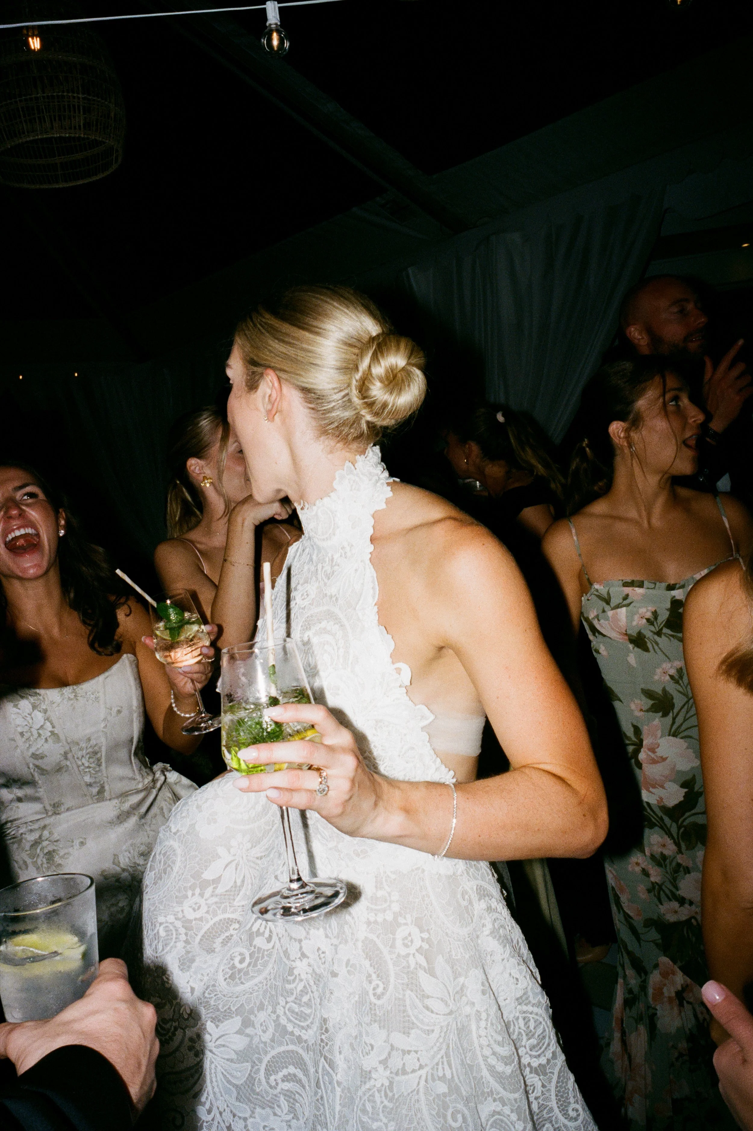 Wedding reception with women dressed in formal attire, holding drinks, laughing and socializing indoors.