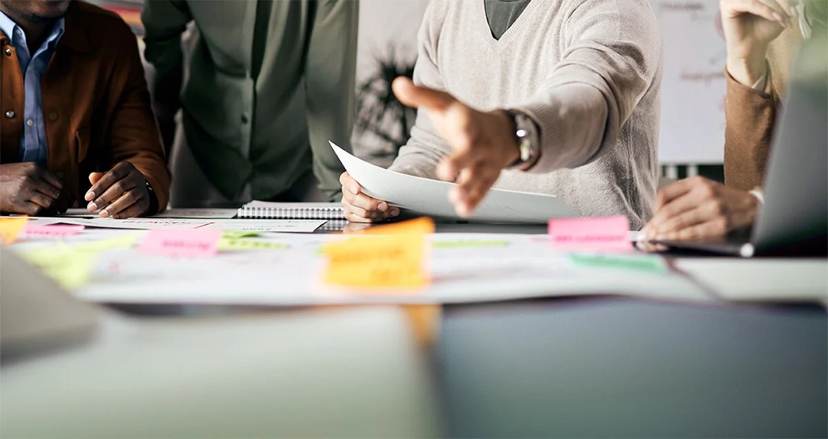 Groupe de personnes en réunion, échangeant des documents et affiches avec des notes colorées sur la table.