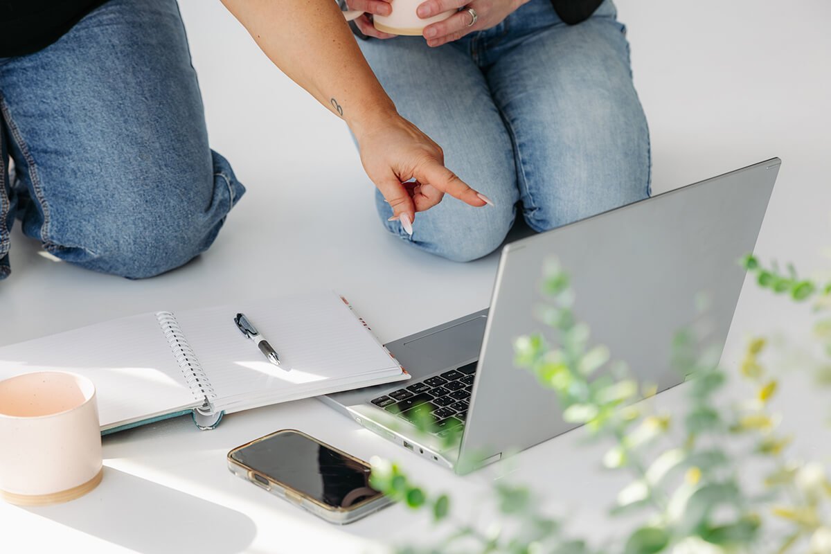 Deux personnes assises par terre avec un ordinateur portable, un cahier, un stylo, un téléphone et une tasse
